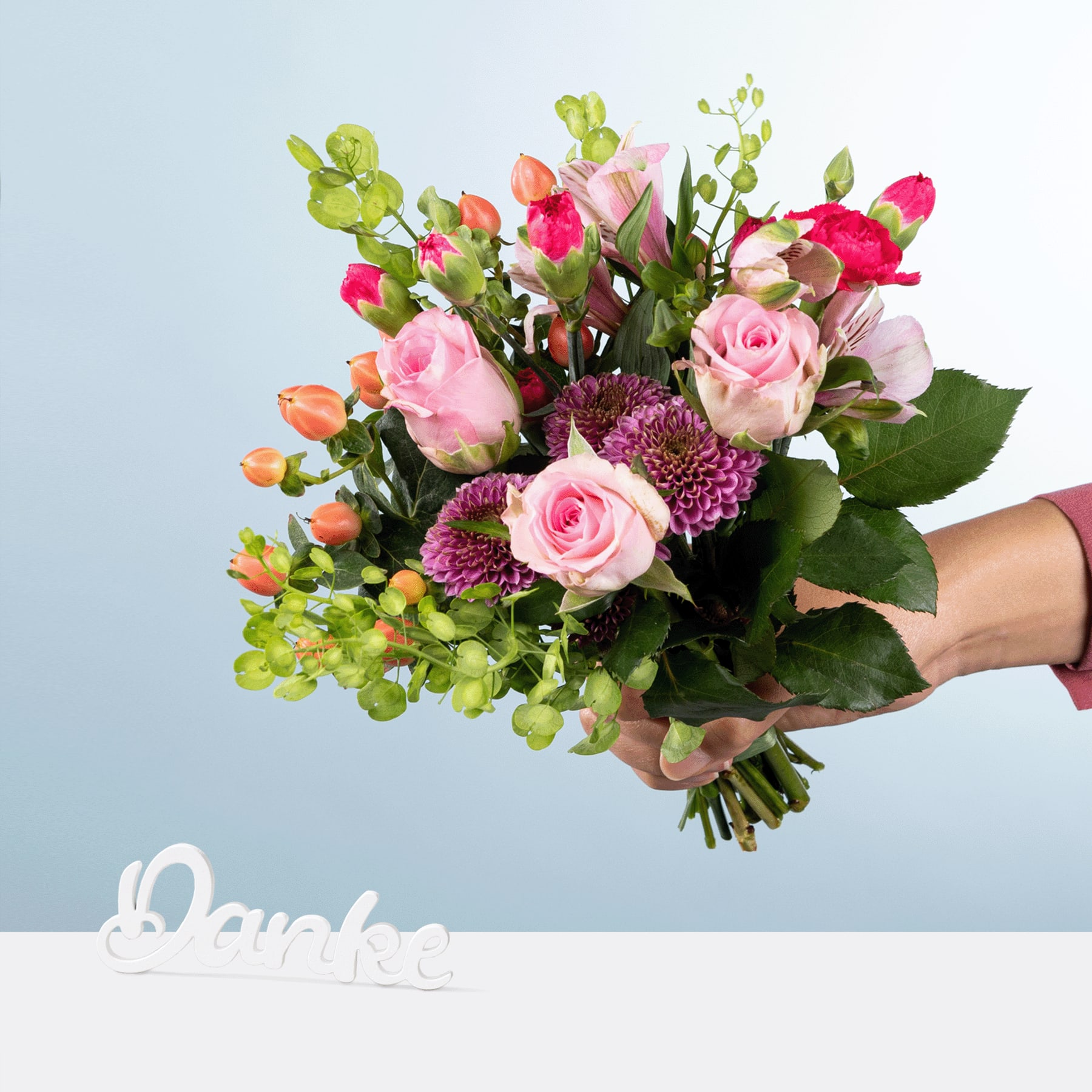 Ein farbenfroher Strauß aus rosa Rosen, violetten Chrysanthemen und grünem Laub wird vor einem schlichten blauen Hintergrund in den Händen einer Person gehalten, im Vordergrund ist das Wort „Danke“ zu sehen.