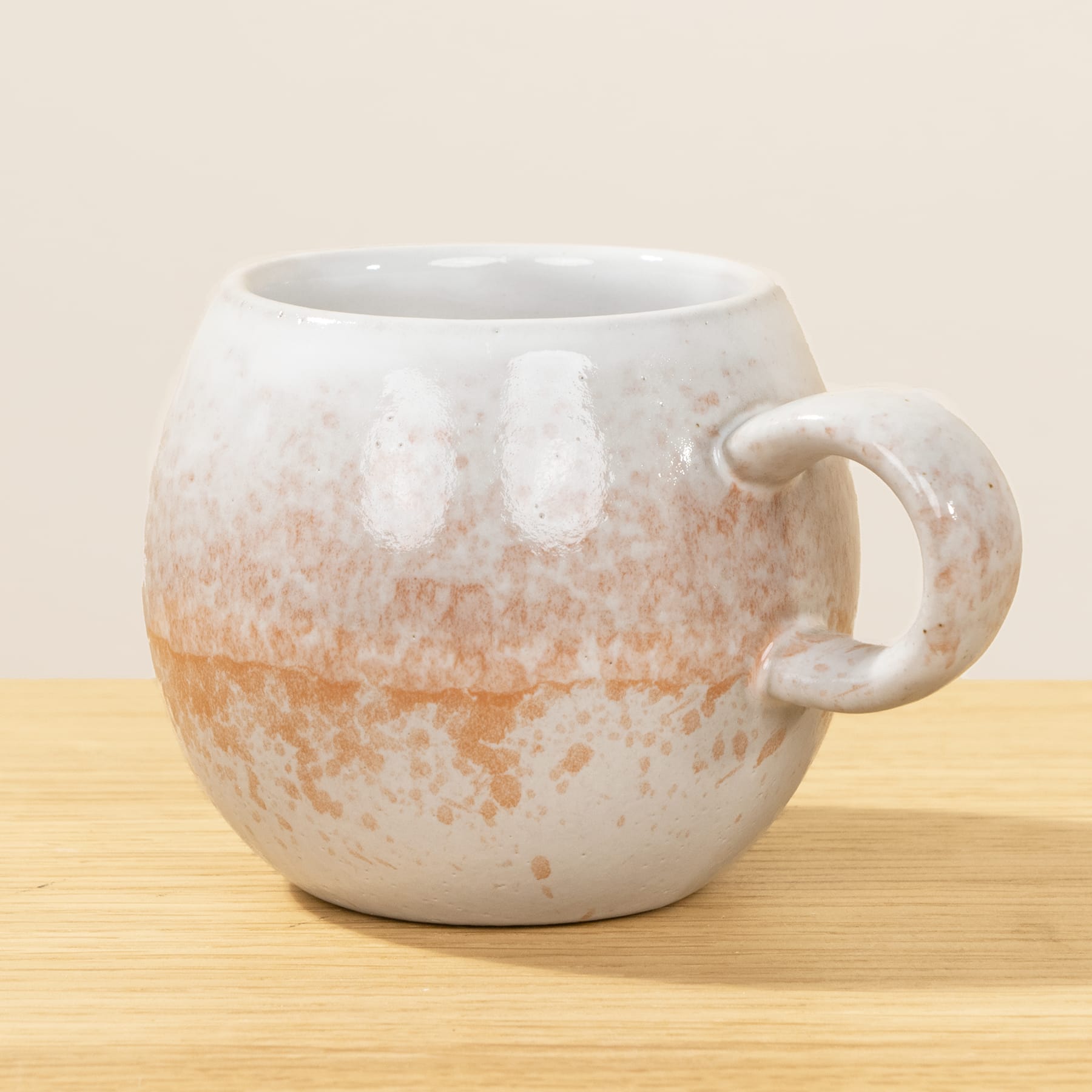 Eine weiße Keramiktasse mit Ombre-Effekt, der von einem hellen Beige zu einem warmen Orangebraun übergeht, steht auf einer Holzoberfläche vor einem schlichten Hintergrund.