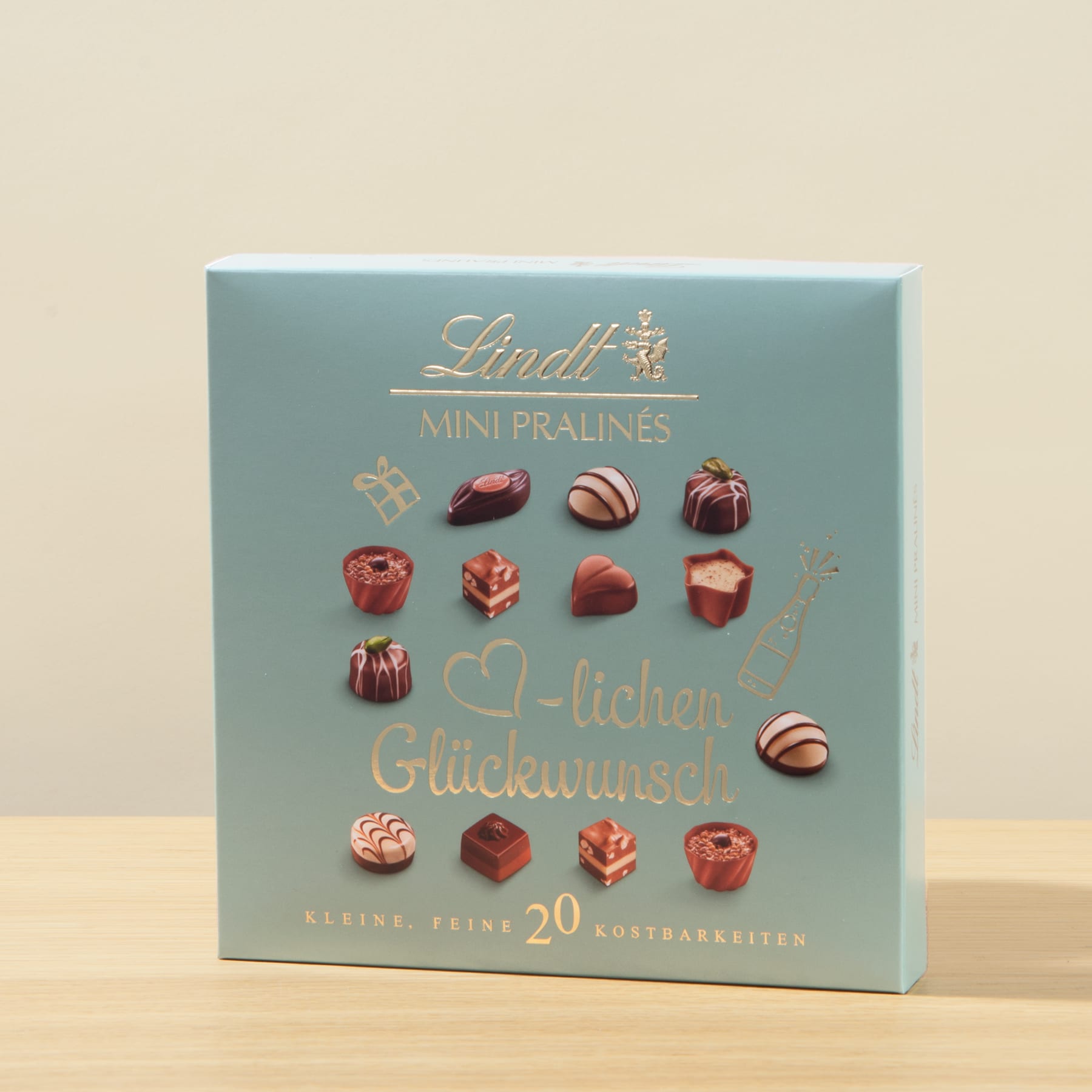 Eine blaue Schachtel mit verschiedenen Schokoladenpralinen, auf deren Vorderseite die Aufschrift „Mini Pralines“ und „Herzlichen Glückwunsch“ aufgedruckt ist.