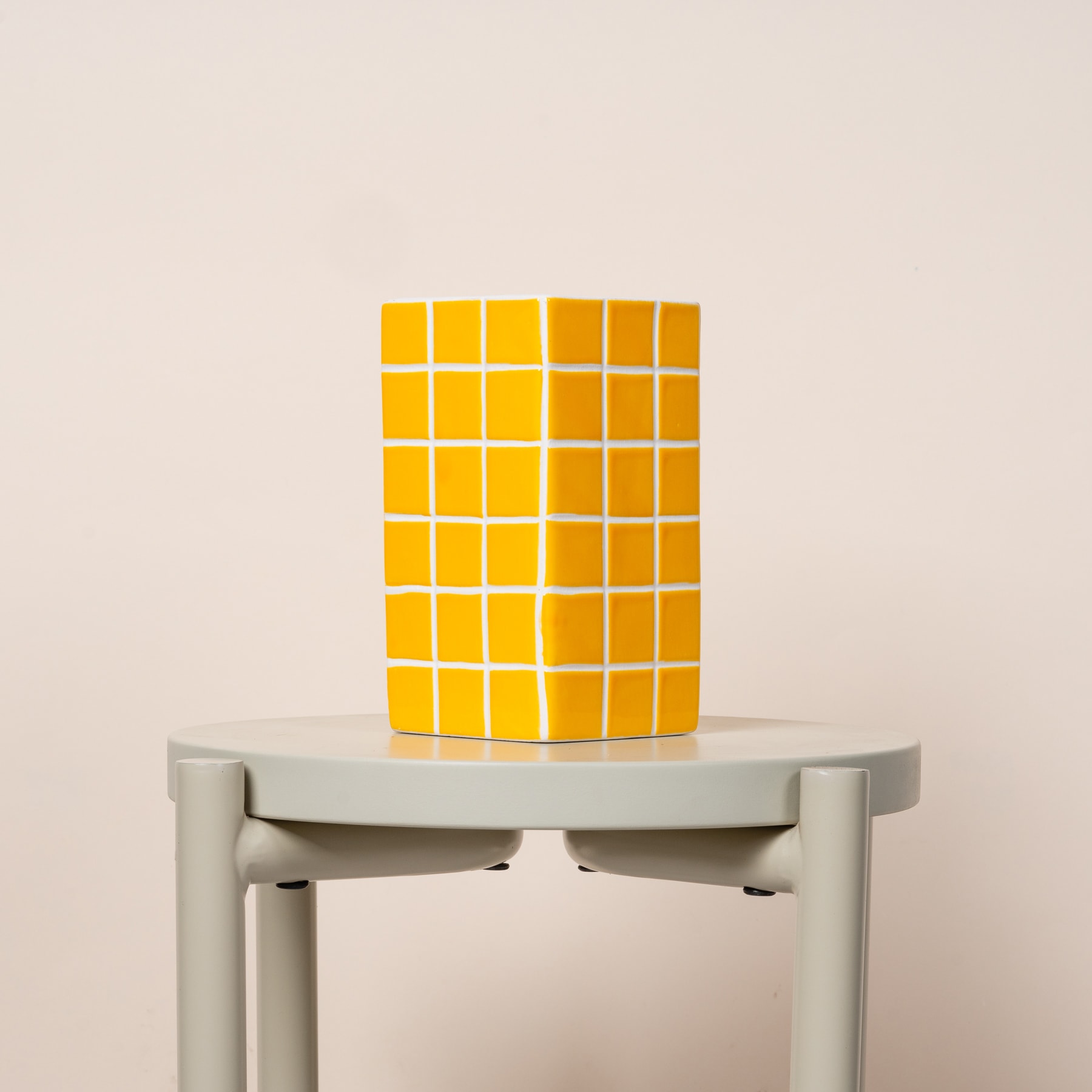 Auf einem grauen Sockel vor hellem Hintergrund wird ein gelbes würfelförmiges Objekt präsentiert.