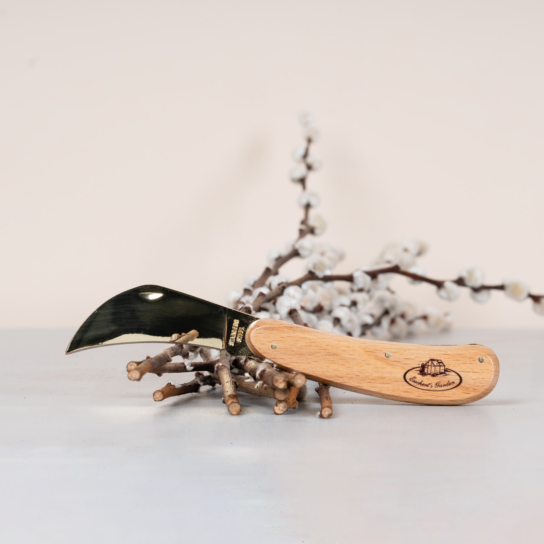 Ein Messer mit Holzgriff liegt auf einer hellen Oberfläche, umgeben von kleinen weißen Blüten oder Knospen, mit einem unscharfen Hintergrund, der wie ein blühender Ast aussieht.