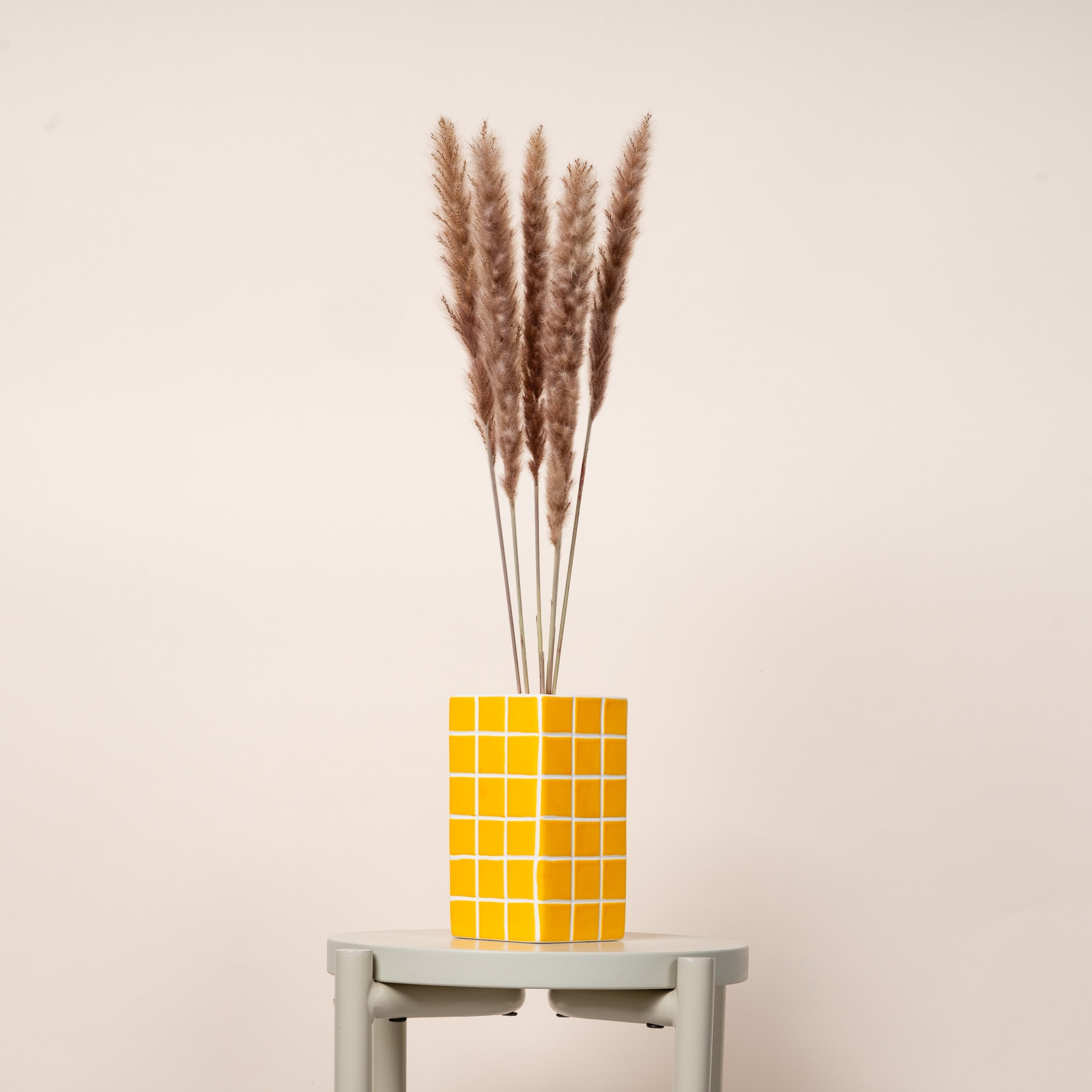 Auf einem grauen Tisch vor beigem Hintergrund steht eine Vase mit getrockneten Weizenhalmen.