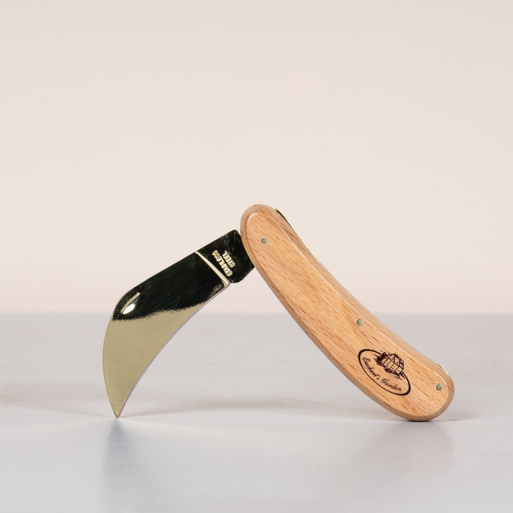 Ein Messer mit Holzgriff und gebogener schwarzer Klinge liegt auf einer hellen Oberfläche vor einem schlichten Hintergrund.