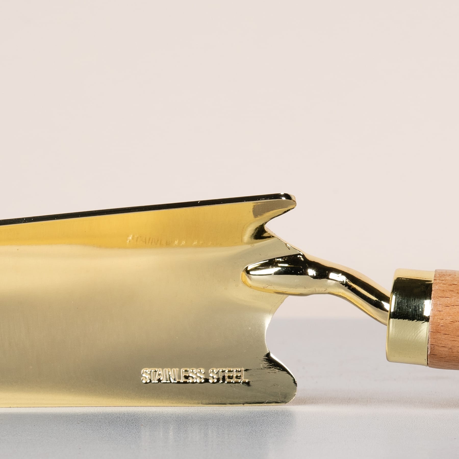 Ein goldfarbener Metallgegenstand, möglicherweise ein Werkzeug oder Utensil, auf dessen Oberfläche vor einem schlichten, hellen Hintergrund der Text „Stainless Steel“ eingraviert ist.