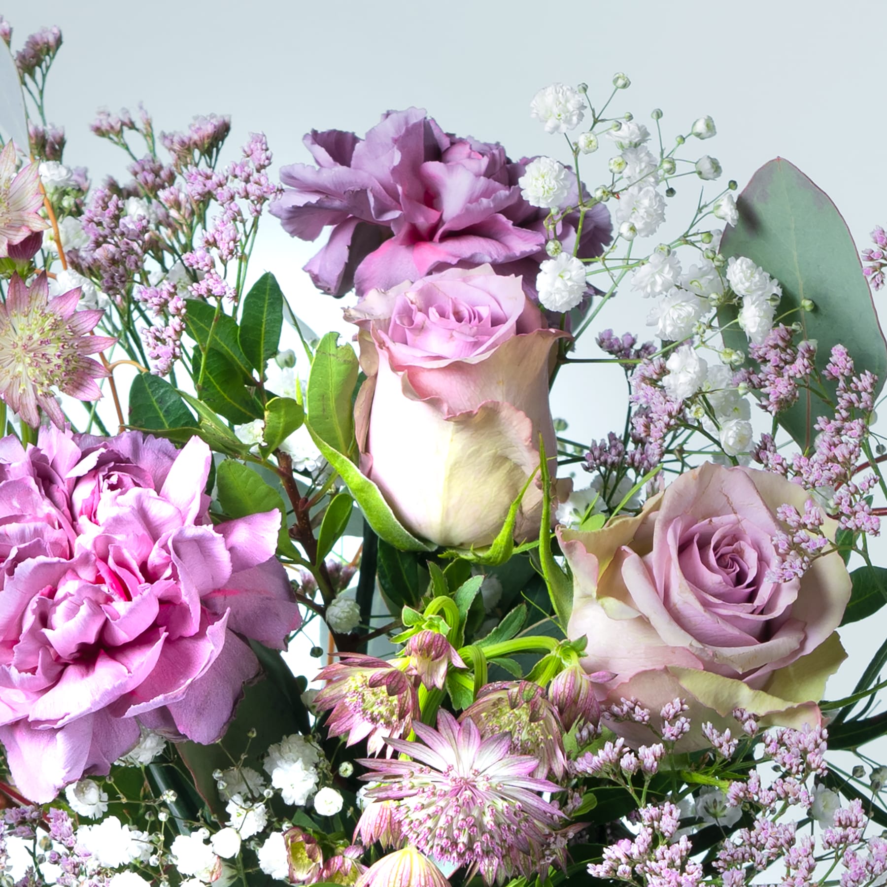 Ein lebendiger Strauß verschiedener rosa und violetter Blumen, darunter Rosen, Pfingstrosen und Schleierkraut, vor einem weichen, unscharfen Hintergrund.