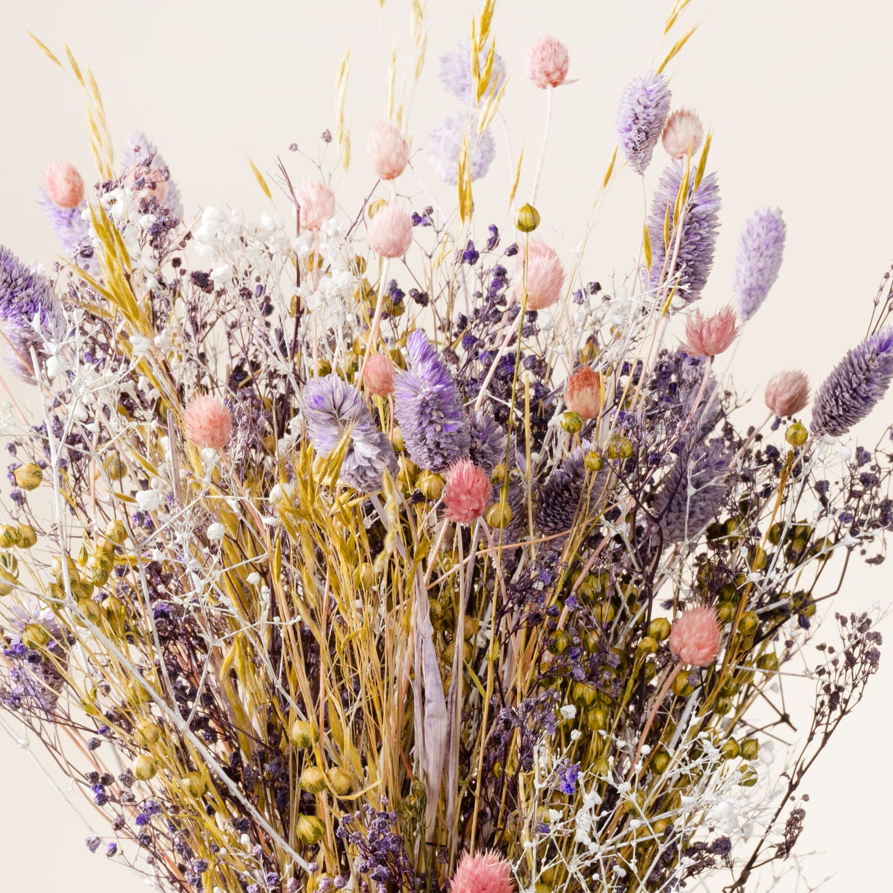 Ein lebendiger Strauß getrockneter Blumen und Pflanzen, darunter Lavendel, Weizenhalme und andere zarte Blüten, füllt den Rahmen mit einer warmen, erdigen Palette vor einem schlichten Hintergrund.