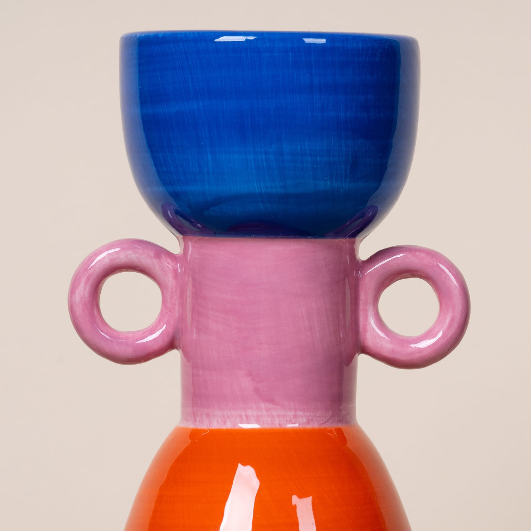 Ein farbenfrohes Keramikgefäß mit einer blauen Schale auf einem rosa und orangefarbenen Sockel vor einem neutralen Hintergrund.