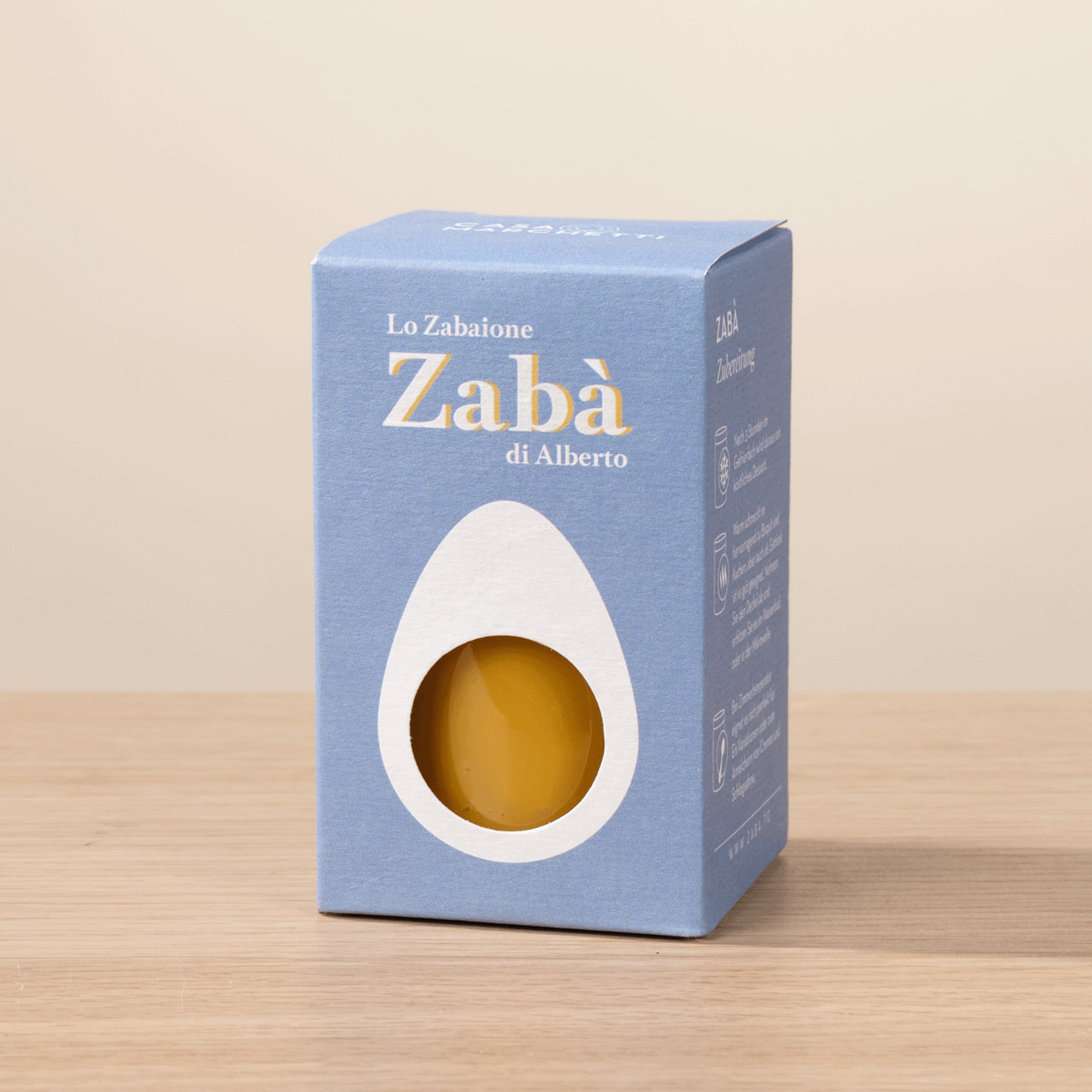 Auf einer Holzoberfläche steht eine blaue Schachtel mit dem Text „Lo Zabalone Zaba di Alberto“ und enthält einen gelben Gegenstand.