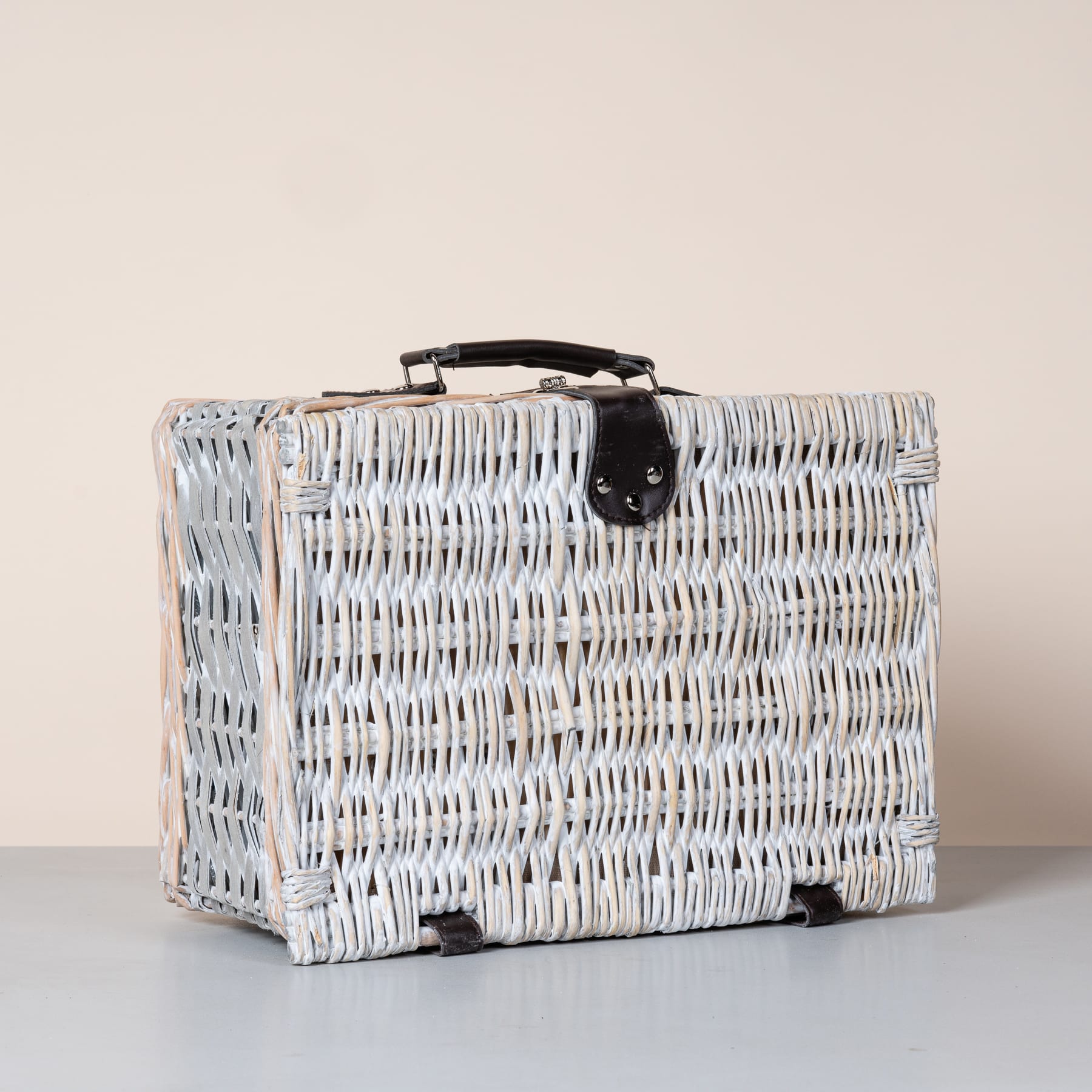 Auf einer hellen Oberfläche steht ein weißer Korbkoffer oder -truhe, dessen kompliziertes Flechtmuster und Metallverschluss sichtbar sind.