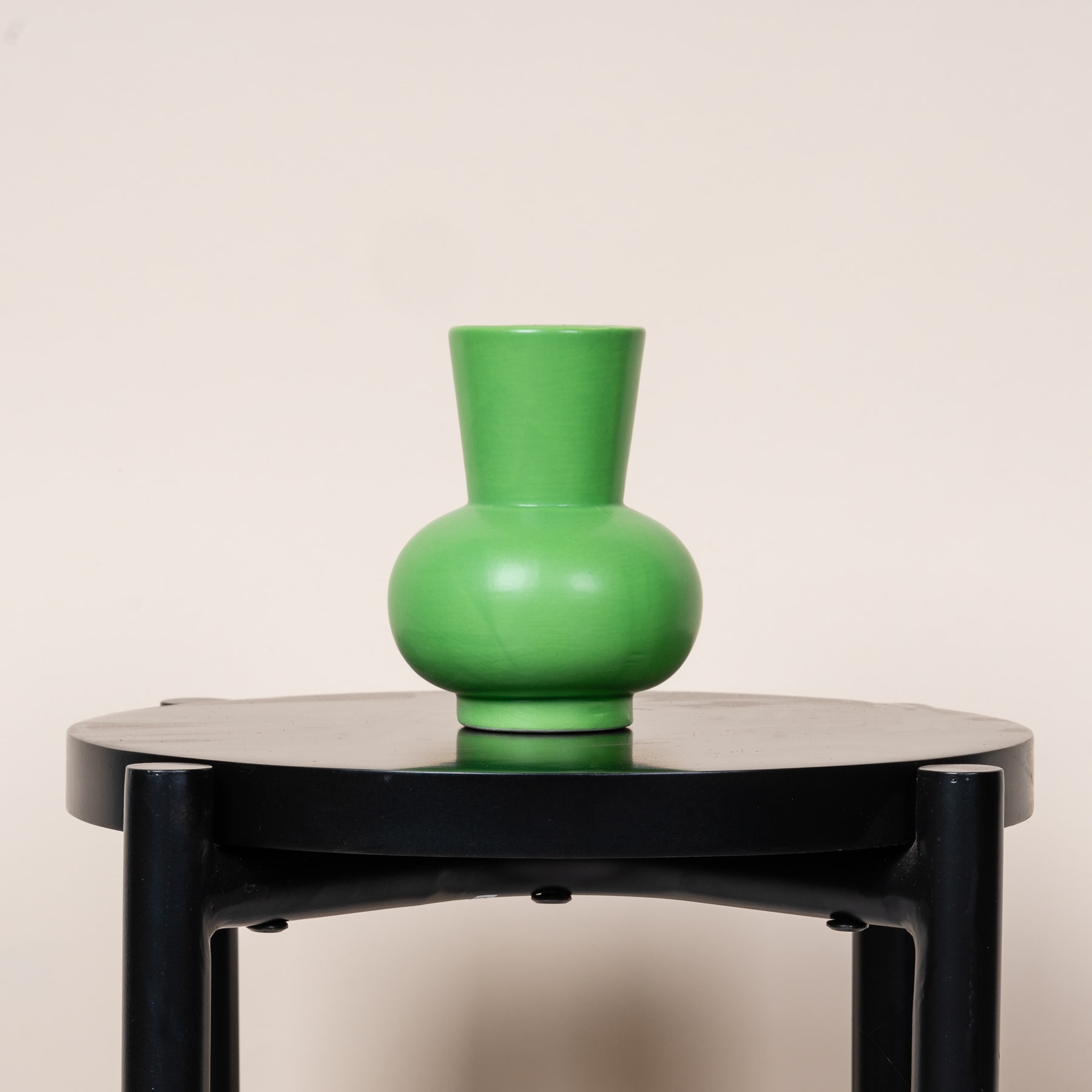 Eine grüne Keramikvase steht auf einer schwarzen runden Plattform vor einem schlichten, hellen Hintergrund.