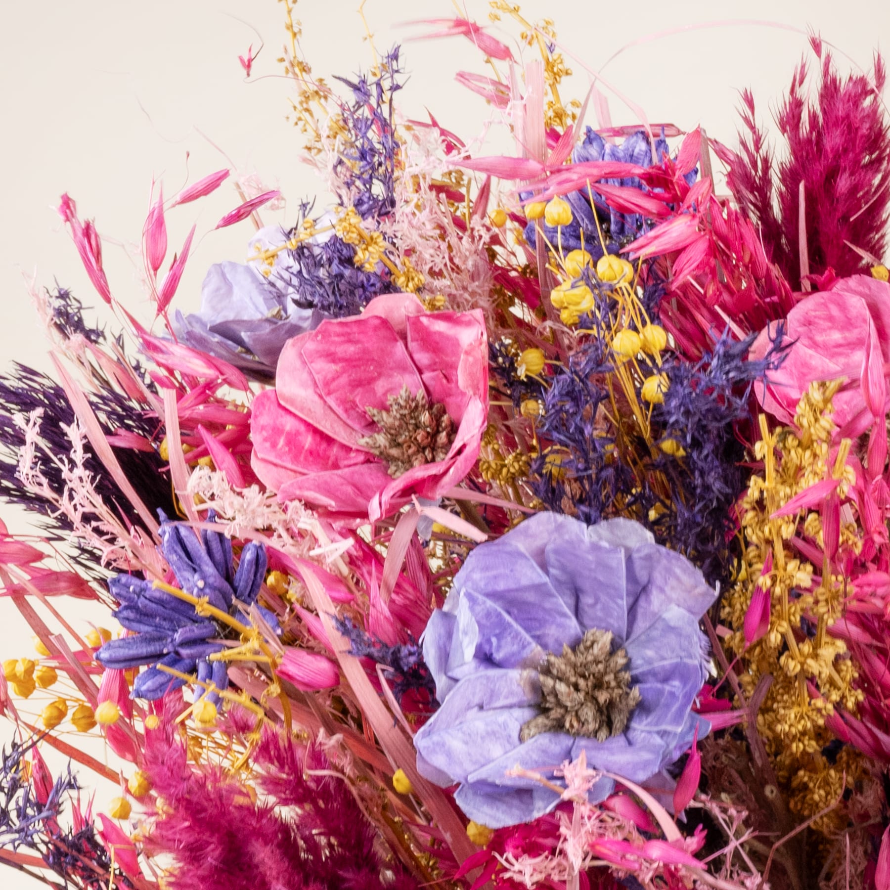 Ein lebendiger Strauß bunter Blumen, darunter rosa Pfingstrosen, violette Schwertlilien und gelbe Mimosen, füllt den Rahmen vor einem weichen, neutralen Hintergrund.