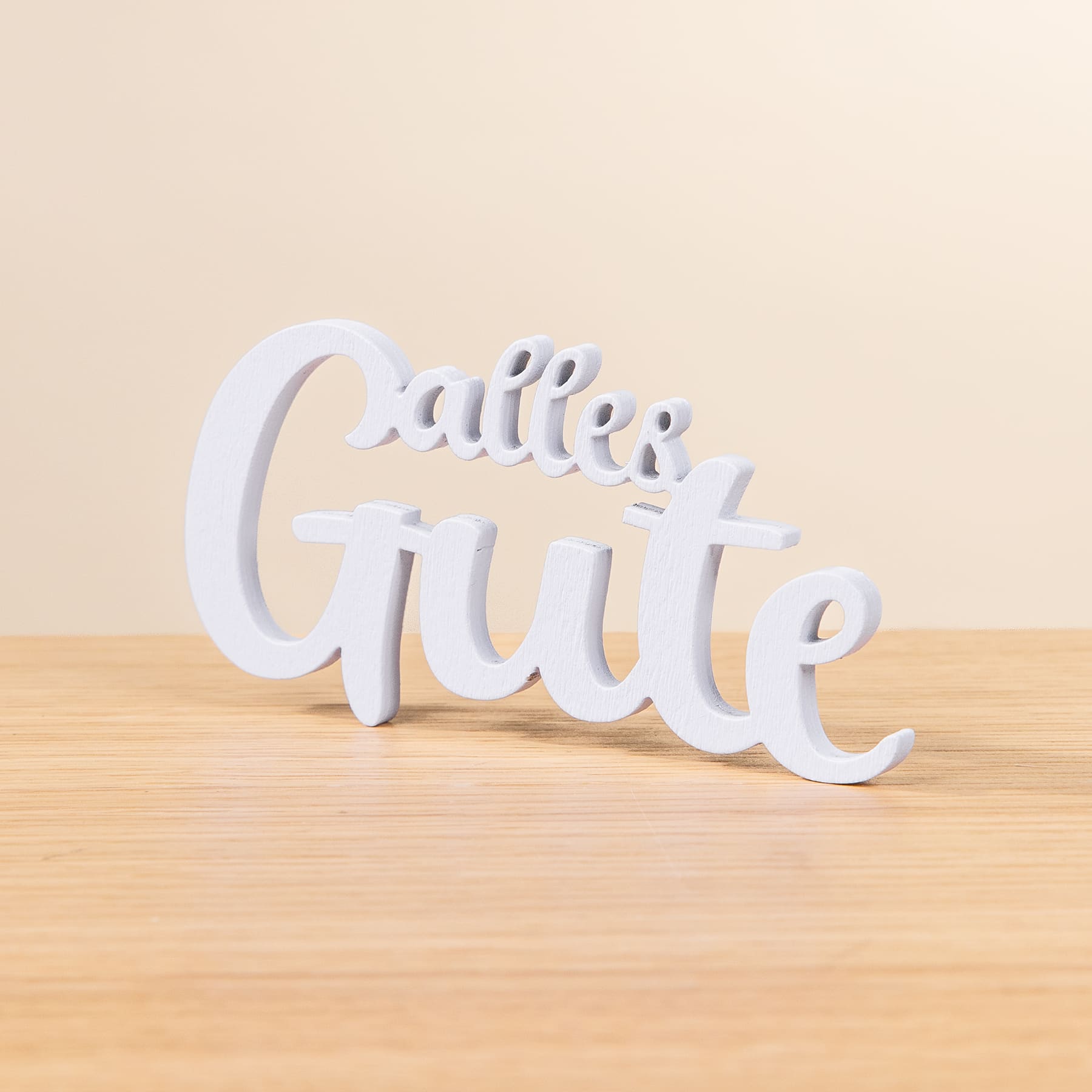 Das Bild zeigt eine weiße, dreidimensionale Textskulptur mit der Aufschrift „Callie Grute“, die auf einer Holzoberfläche vor einem hellen Hintergrund platziert ist.