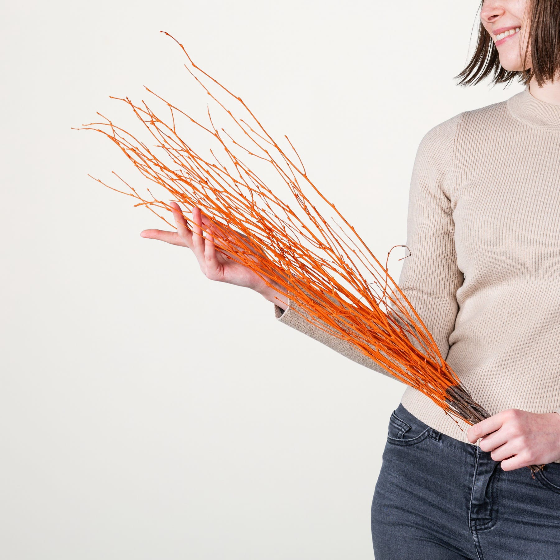Eine Person hält ein Bündel leuchtend orangefarbener Zweige oder Äste vor einem schlichten weißen Hintergrund.