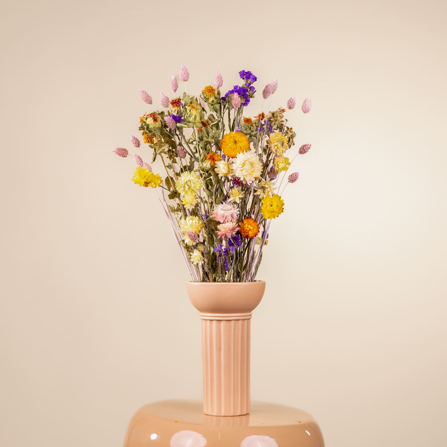 Ein Strauß lebendiger, farbenfroher Wildblumen in einer einfachen Keramikvase steht vor einem schlichten, beigen Hintergrund.