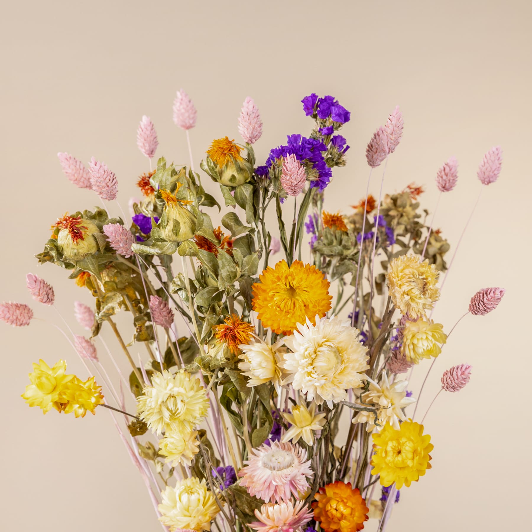 Ein lebendiger Strauß verschiedener bunter Blumen, darunter Gänseblümchen, Chrysanthemen und andere Blüten, arrangiert vor einem neutralen beigen Hintergrund.