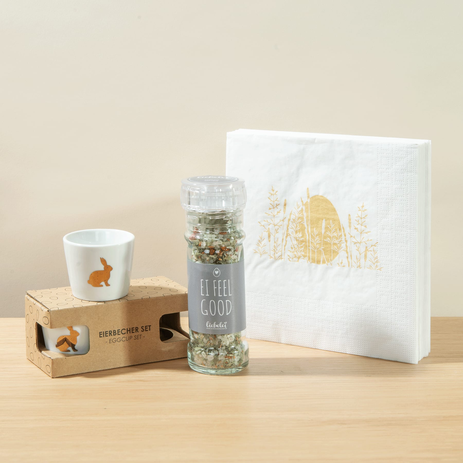 Das Bild zeigt eine Holzkiste mit dem Aufdruck „Evergreen Joy“, einen Glasbehälter, der scheinbar mit Gewürzen oder Kräutern gefüllt ist, und eine weiße Keramiktasse mit einem Eichhörnchenmuster, alles auf einer Holzoberfläche mit hellem Hintergrund.