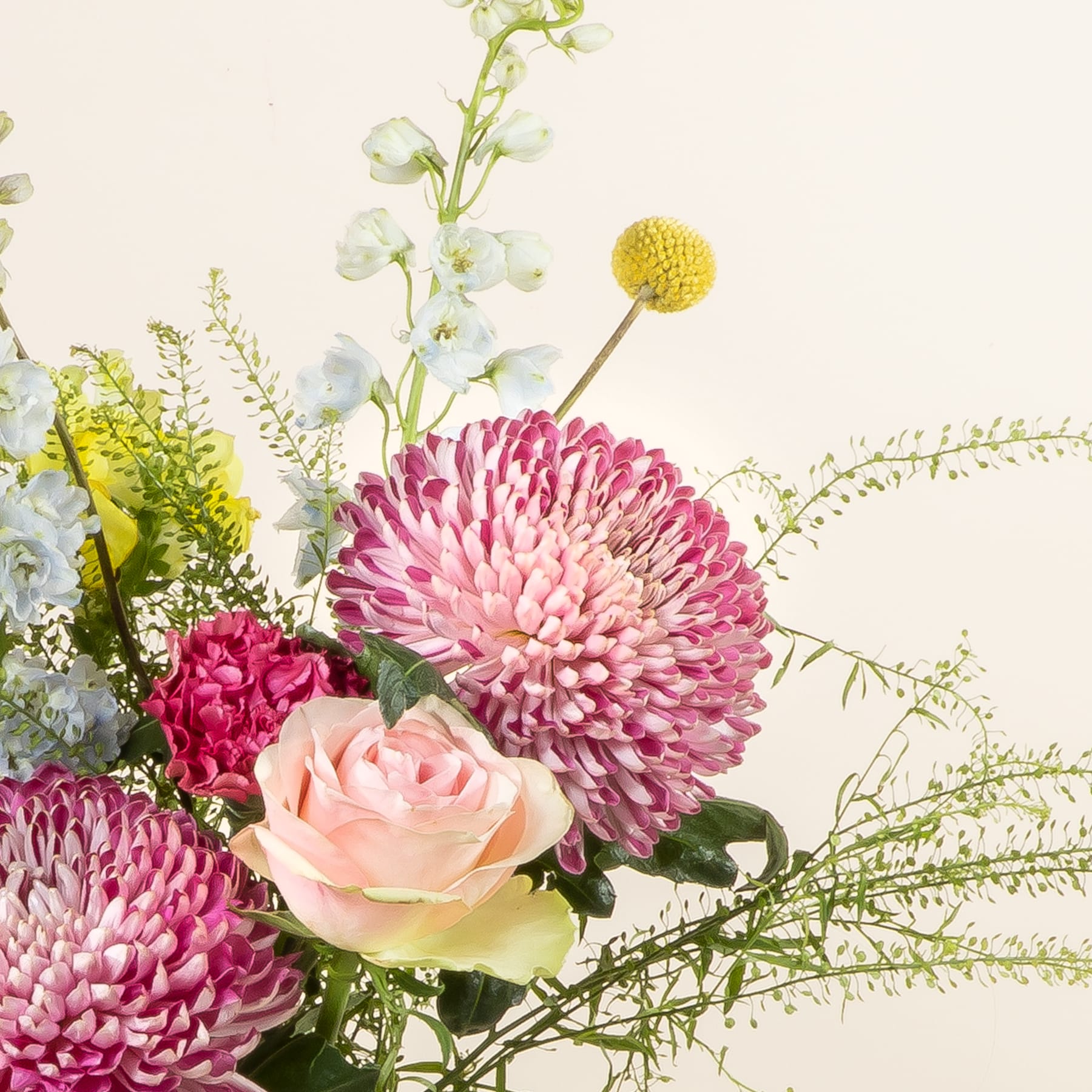 Ein lebendiger Strauß aus rosa Chrysanthemen, pfirsichfarbenen Rosen und gelben Knopfblumen vor einem weichen, neutralen Hintergrund.