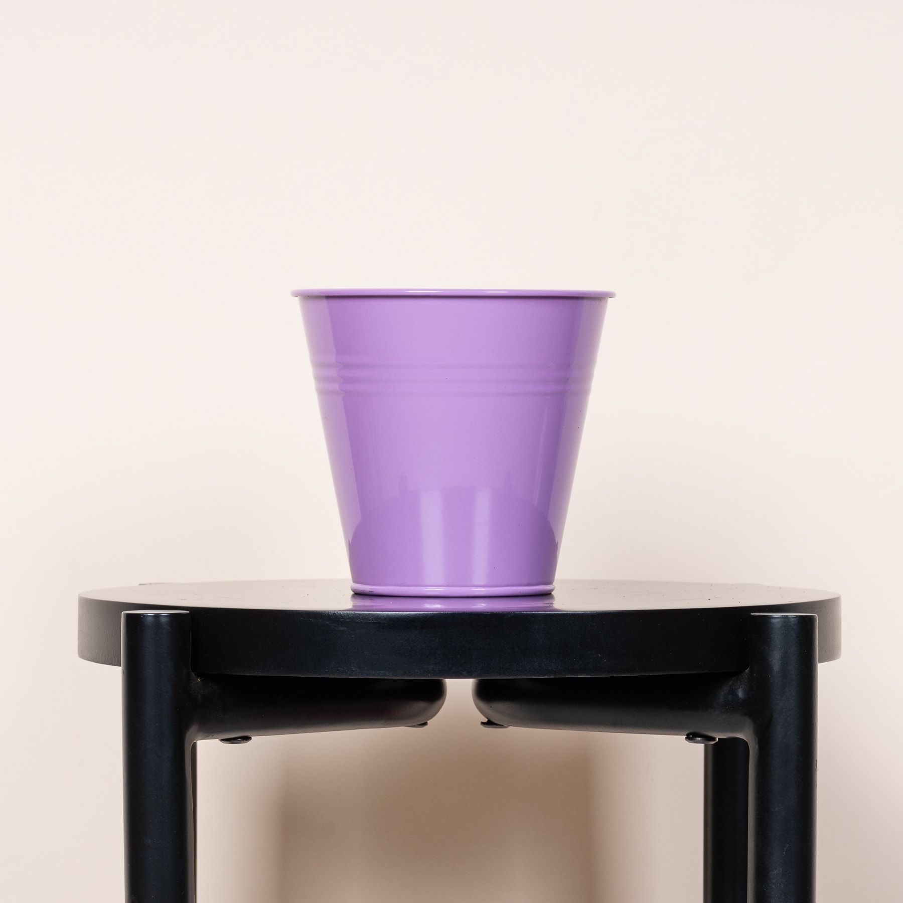 Ein violetter Plastikbecher steht auf einem schwarzen Metallständer vor einem schlichten, hellen Hintergrund.
