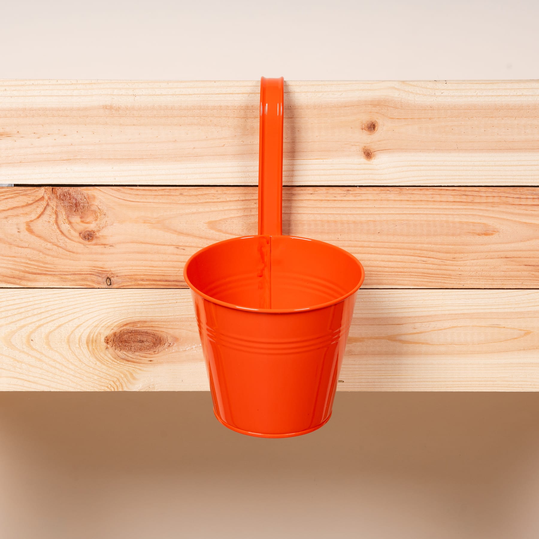 An einer Holzwand hängt ein leuchtend orangefarbener Plastikbecher, im Hintergrund sind die Holzbretter zu sehen.