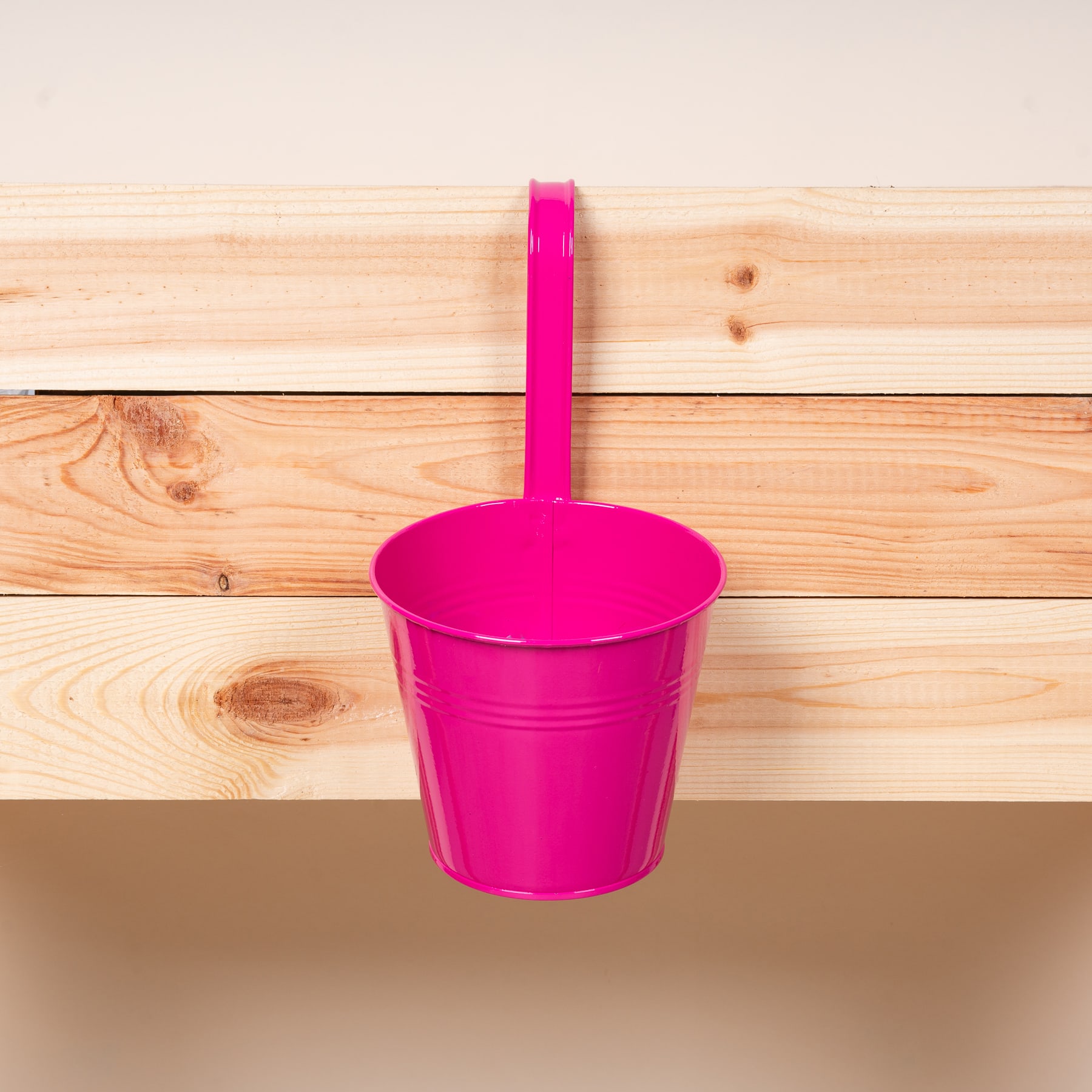 Ein leuchtend rosa Metalleimer oder -behälter hängt auf einem Holzbretthintergrund.