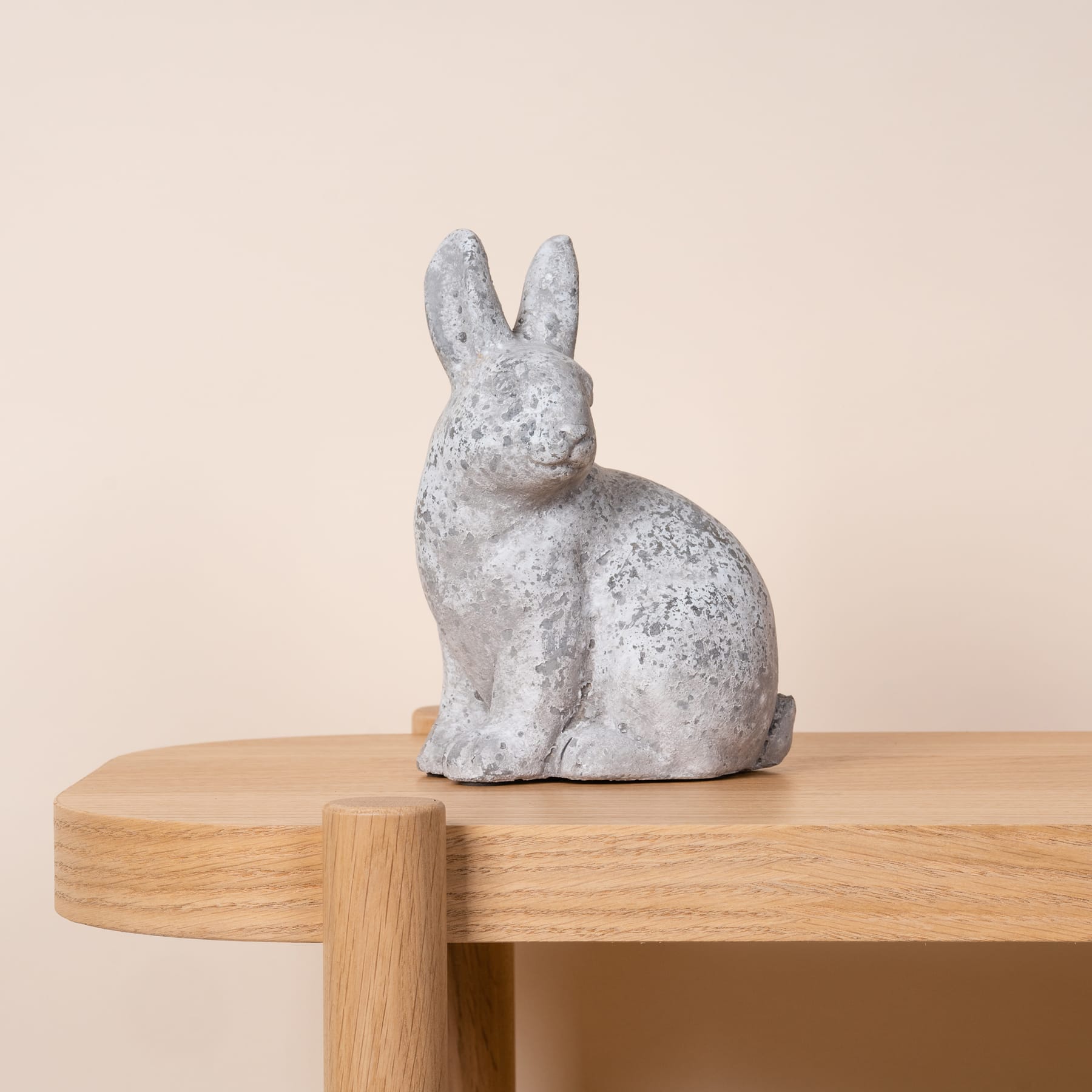 Eine gesprenkelte Kaninchenfigur aus Keramik sitzt auf einer Holzplattform vor einem hellen Hintergrund.