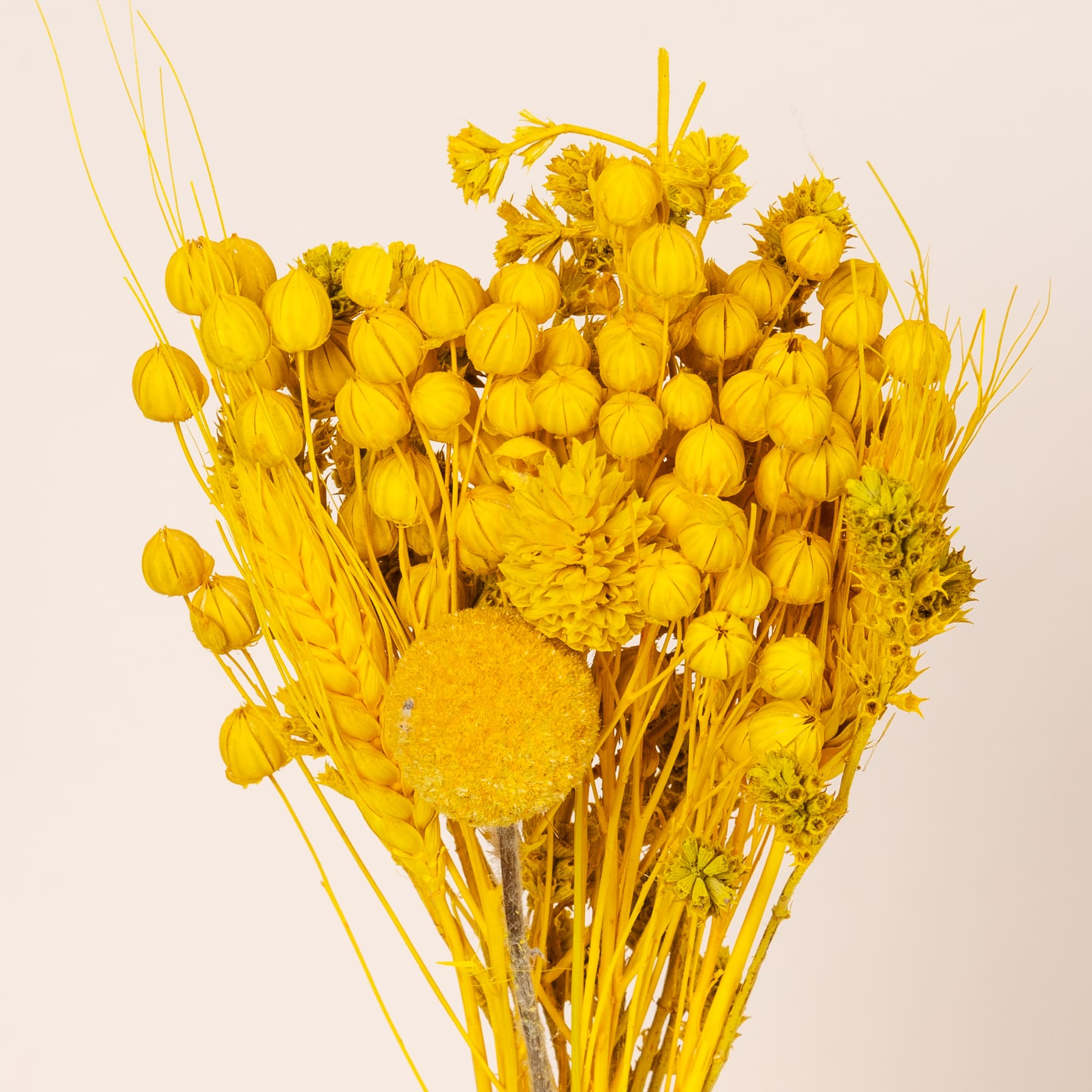 Ein lebendiger Strauß verschiedener gelber Blumen, darunter Chrysanthemen, Ringelblumen und andere Blüten, arrangiert in einer auffälligen herzförmigen Komposition vor einem schlichten, hellen Hintergrund.