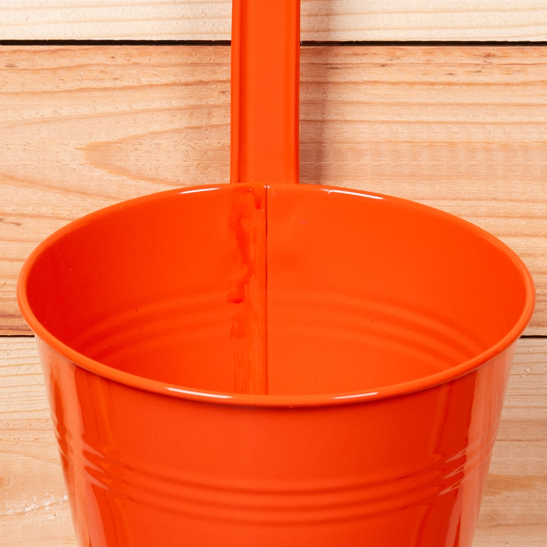 Ein leuchtend orangefarbener Metalleimer oder -behälter steht auf einer Holzoberfläche.