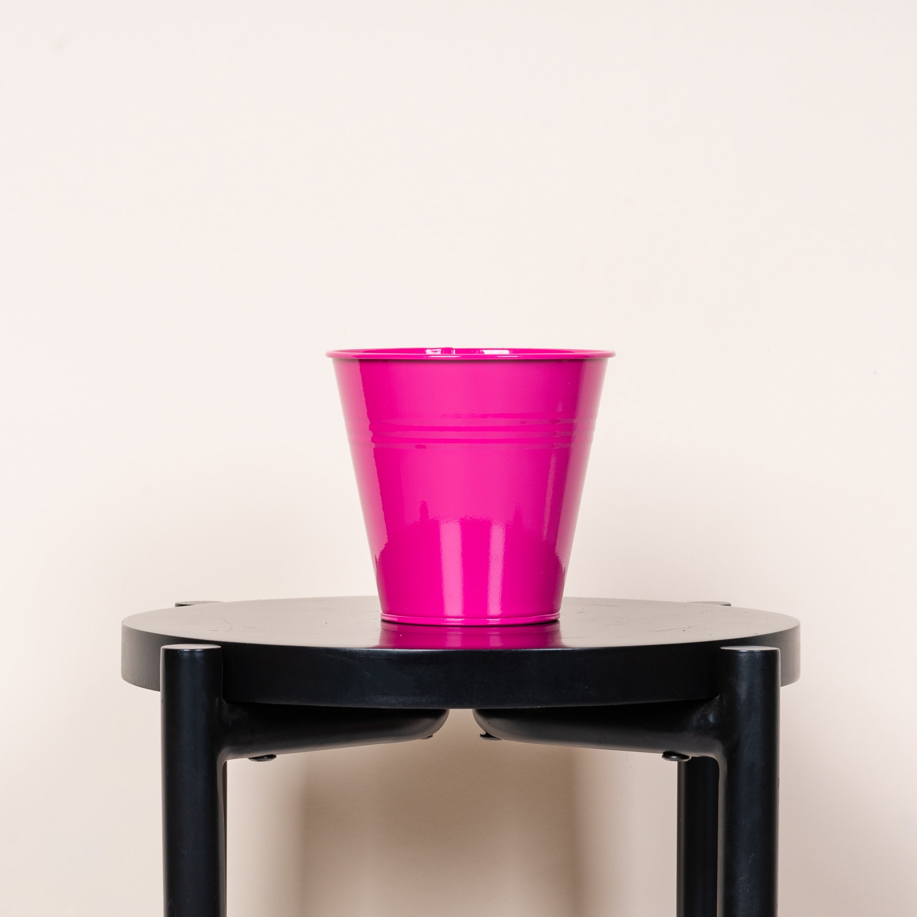 Auf einem schwarzen, minimalistischen Beistelltisch steht vor einem schlichten, hellen Hintergrund ein leuchtend rosa Plastikbecher.