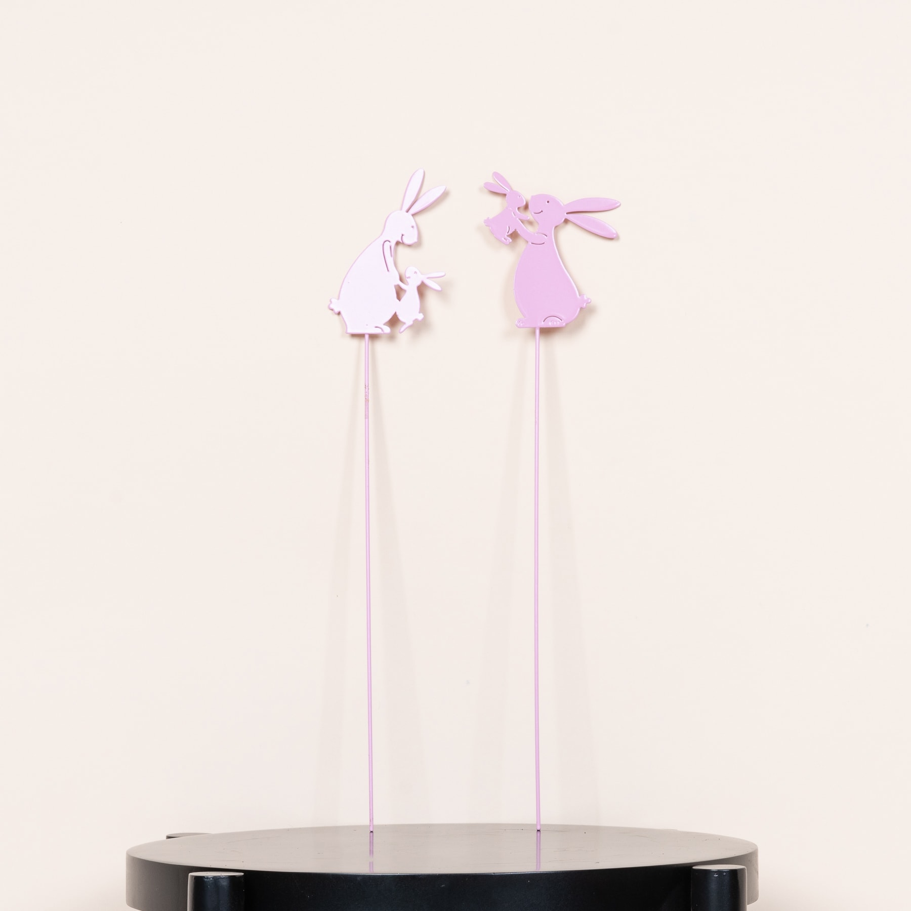 Das Bild zeigt zwei zarte, rosa Papierfiguren – eine Ballerina und einen Schmetterling – die an dünnen Stäben vor einem schlichten, hellen Hintergrund aufgehängt sind.