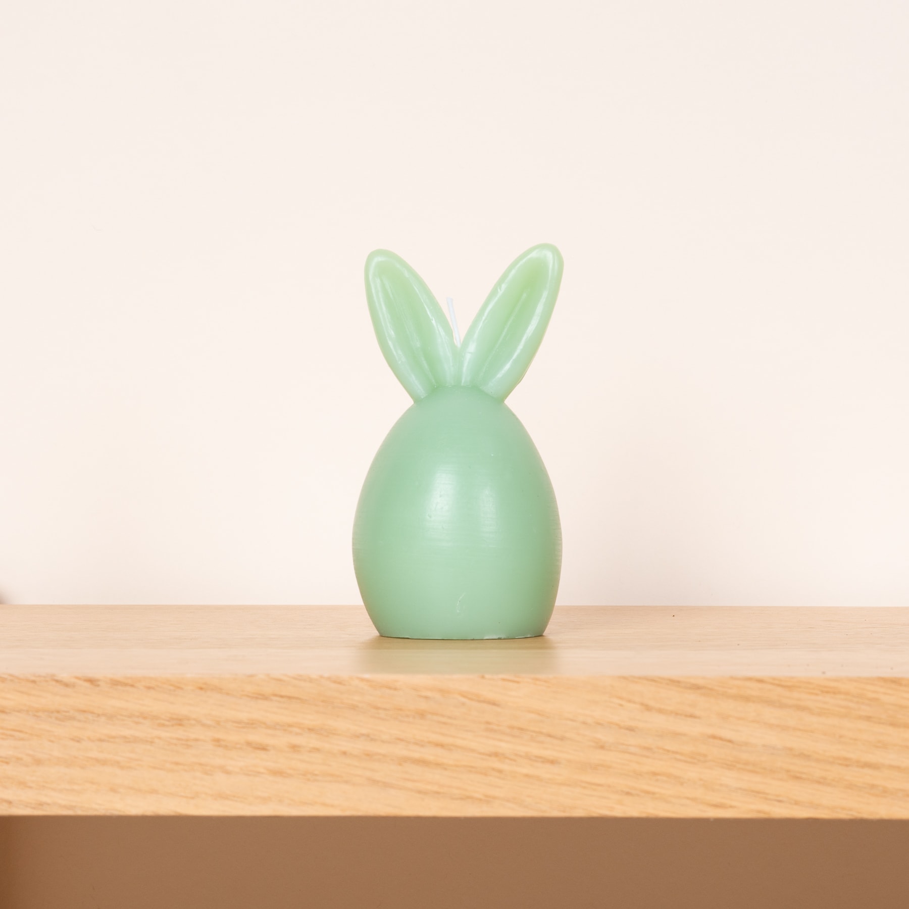 Eine mintgrüne Kaninchenfigur aus Keramik sitzt auf einer Holzoberfläche vor einem schlichten, hellen Hintergrund.