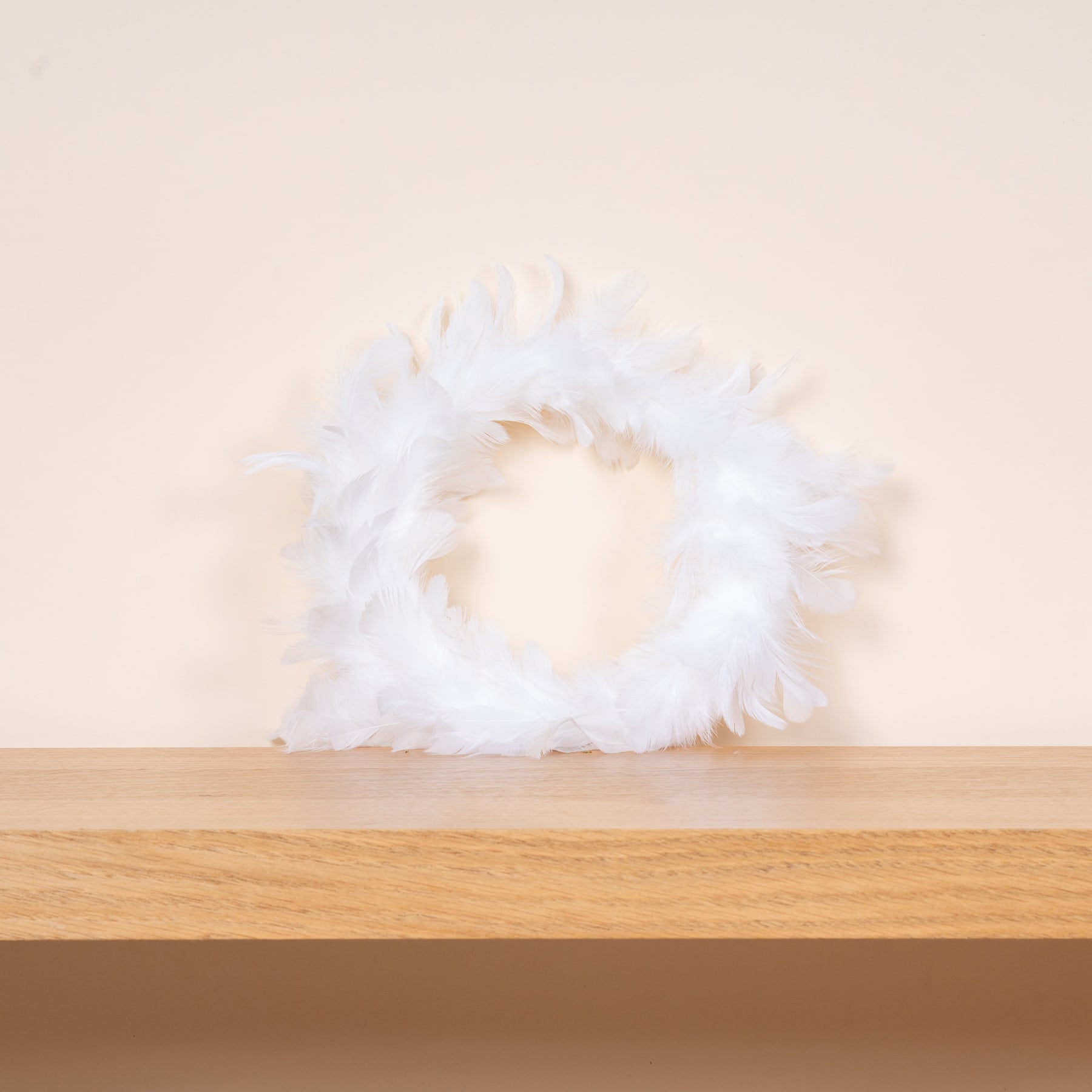 Ein flauschiges, weißes, gefiedertes Objekt liegt auf einer Holzoberfläche vor einem schlichten, hellen Hintergrund.