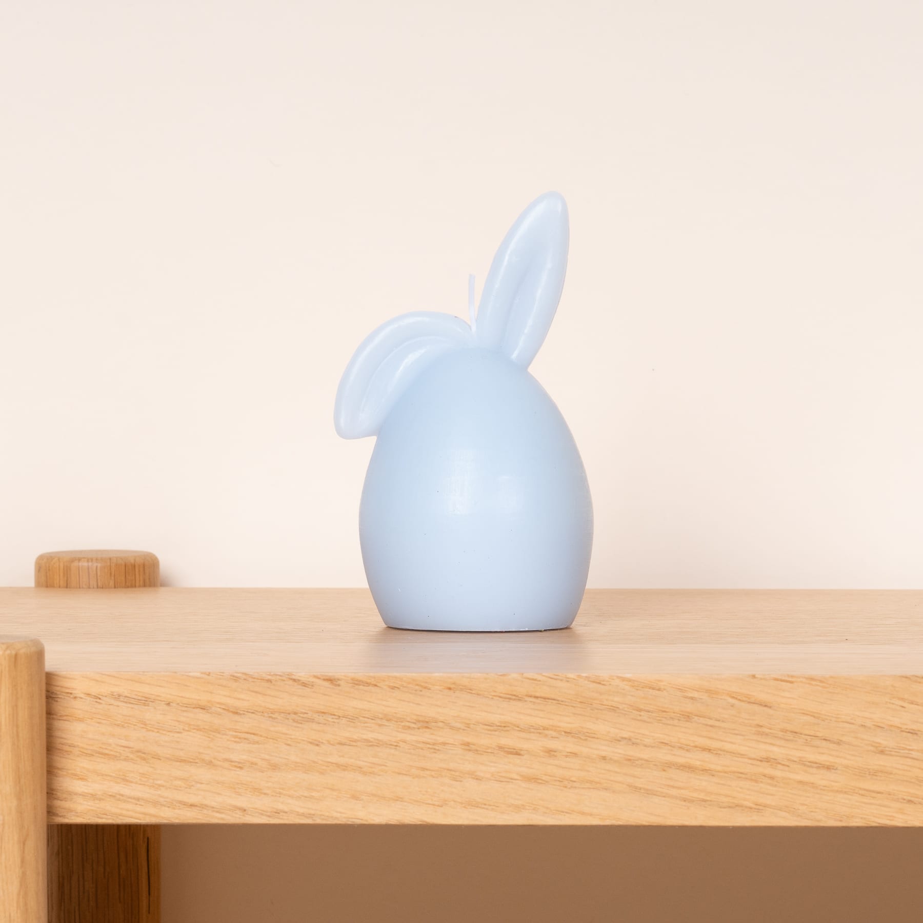 Eine hellblaue Kaninchenfigur aus Keramik steht auf einem Holztisch vor einem schlichten beigen Hintergrund.