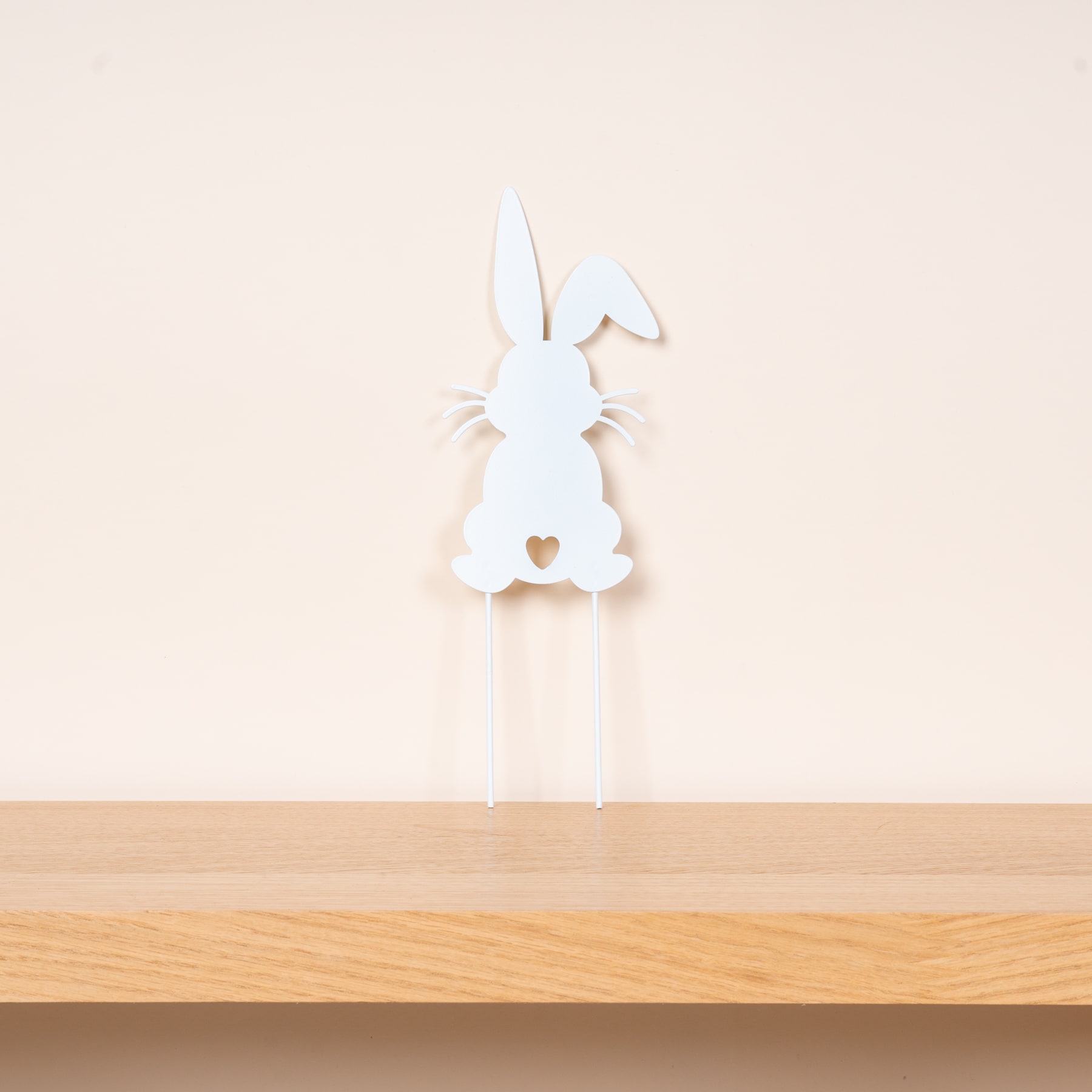 Die weiße Silhouette einer kaninchenähnlichen Figur steht auf einer Holzoberfläche vor einem schlichten, hellen Hintergrund.