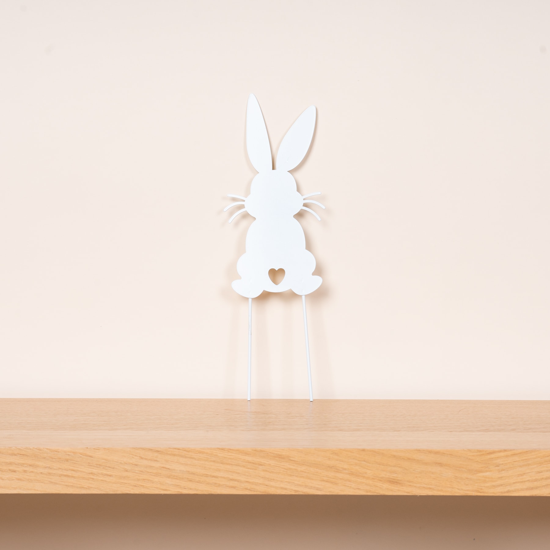 Auf einer Holzfläche steht vor hellem Hintergrund die weiße Silhouette eines Kaninchens.