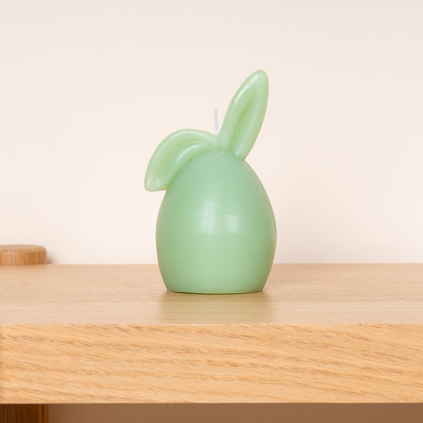 Eine grüne Kaninchenfigur aus Keramik sitzt auf einem Holztisch vor einem hellen Hintergrund.