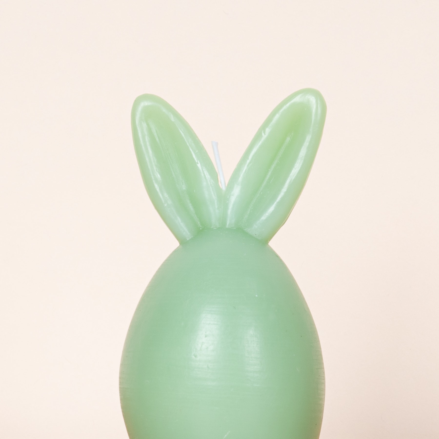 Ein grüner Ballon in Form eines Hasenkopfes vor einem hellbeigen Hintergrund.
