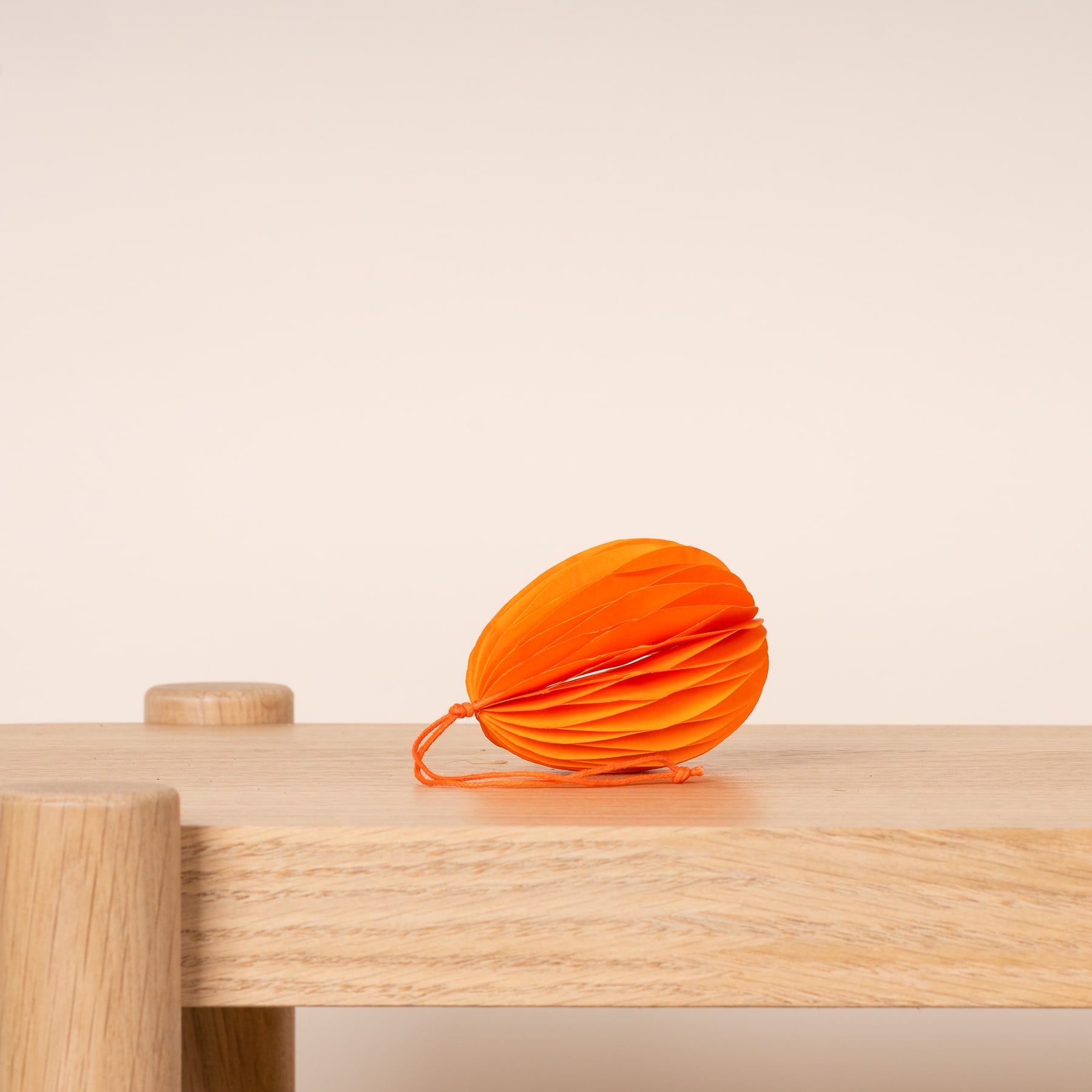 Ein leuchtend orangefarbenes, stoffähnliches Objekt liegt auf einer Holzoberfläche, im Hintergrund sind einfache Holzklötze zu sehen.