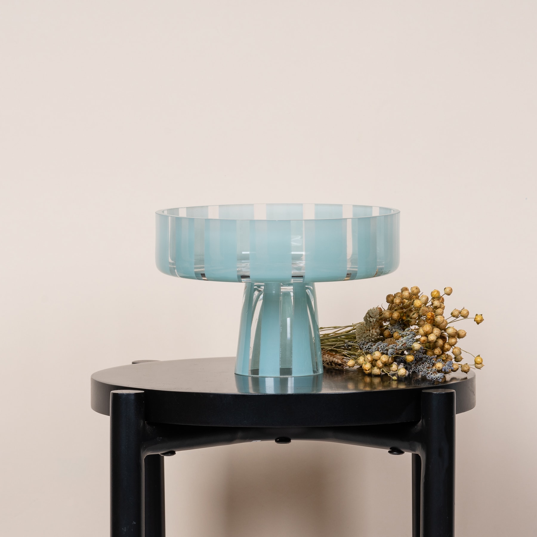 Auf einem schwarzen Tisch vor einem neutralen Hintergrund steht ein Glassockel mit einem Blumenarrangement.