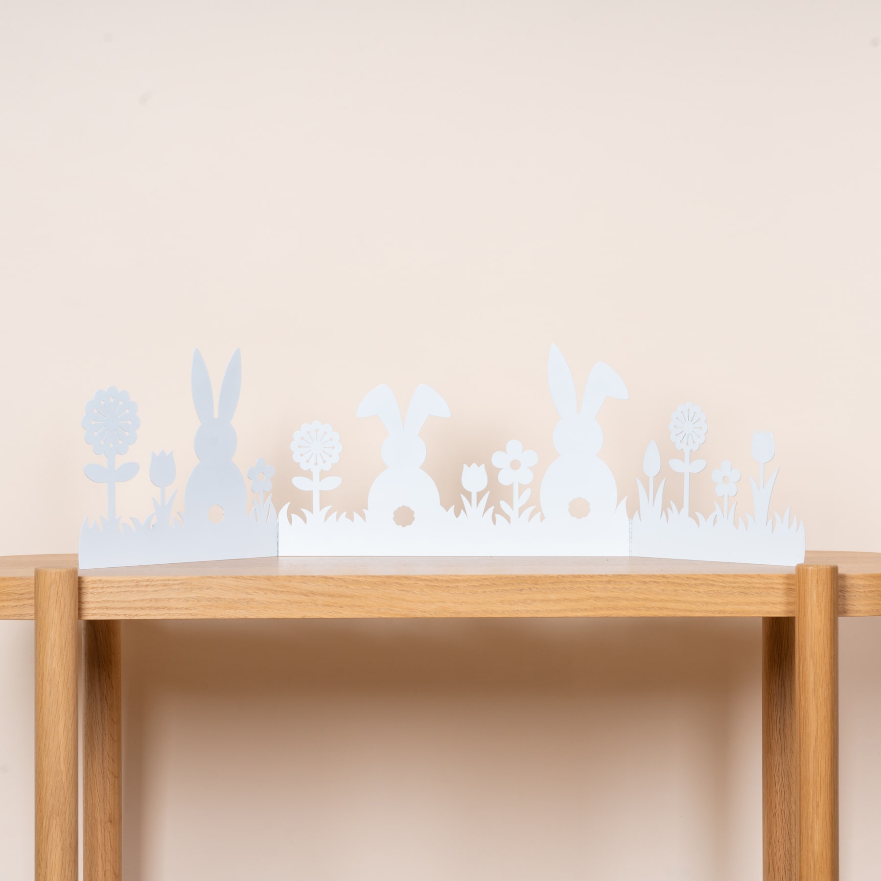 Ein Holzregal mit verschiedenen Silhouetten, darunter Kaninchen, Blumen und andere von der Natur inspirierte Designs, vor einem hellen Hintergrund.