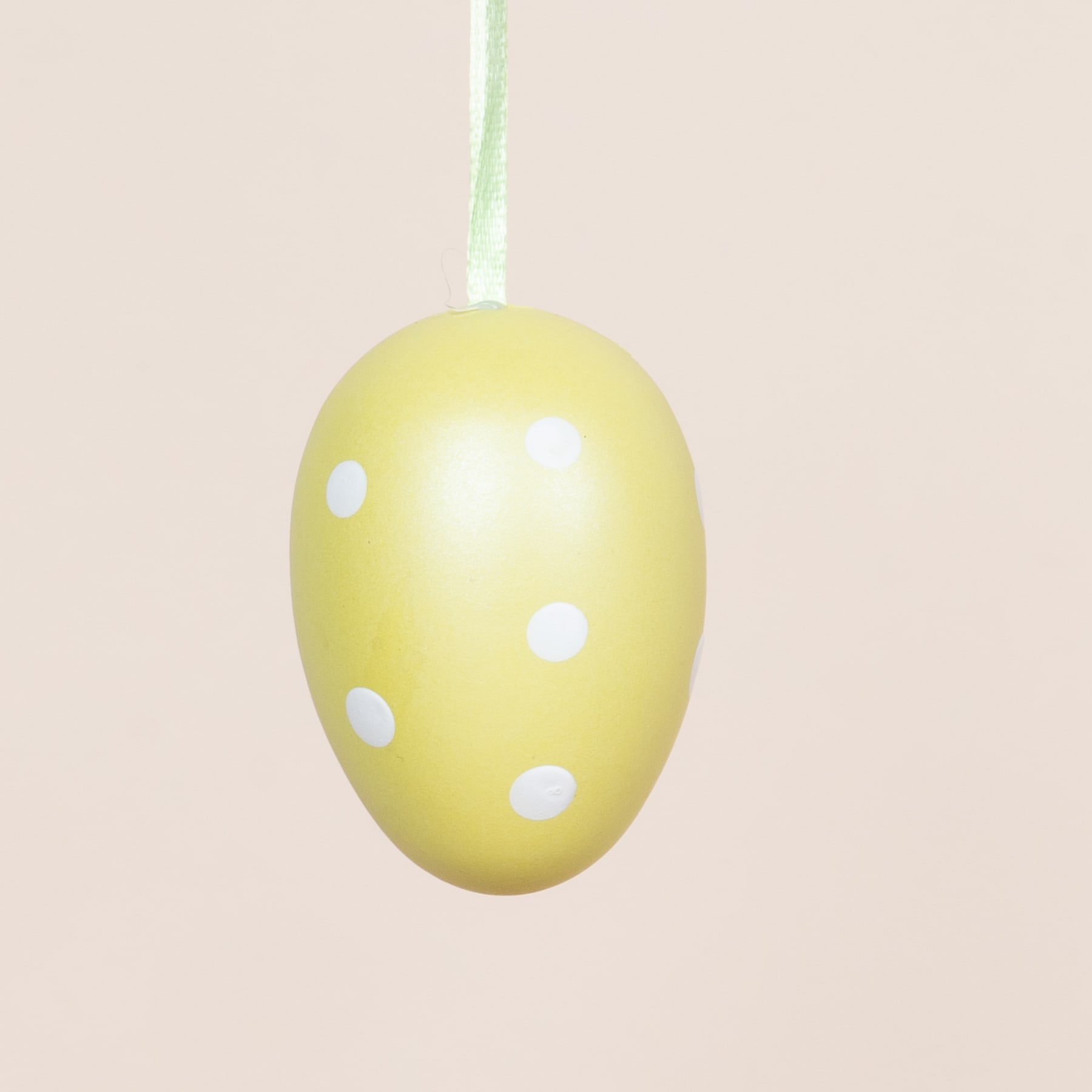 Vor einem hellbeigen Hintergrund hängt ein gelbes Osterei mit weißen Punkten.