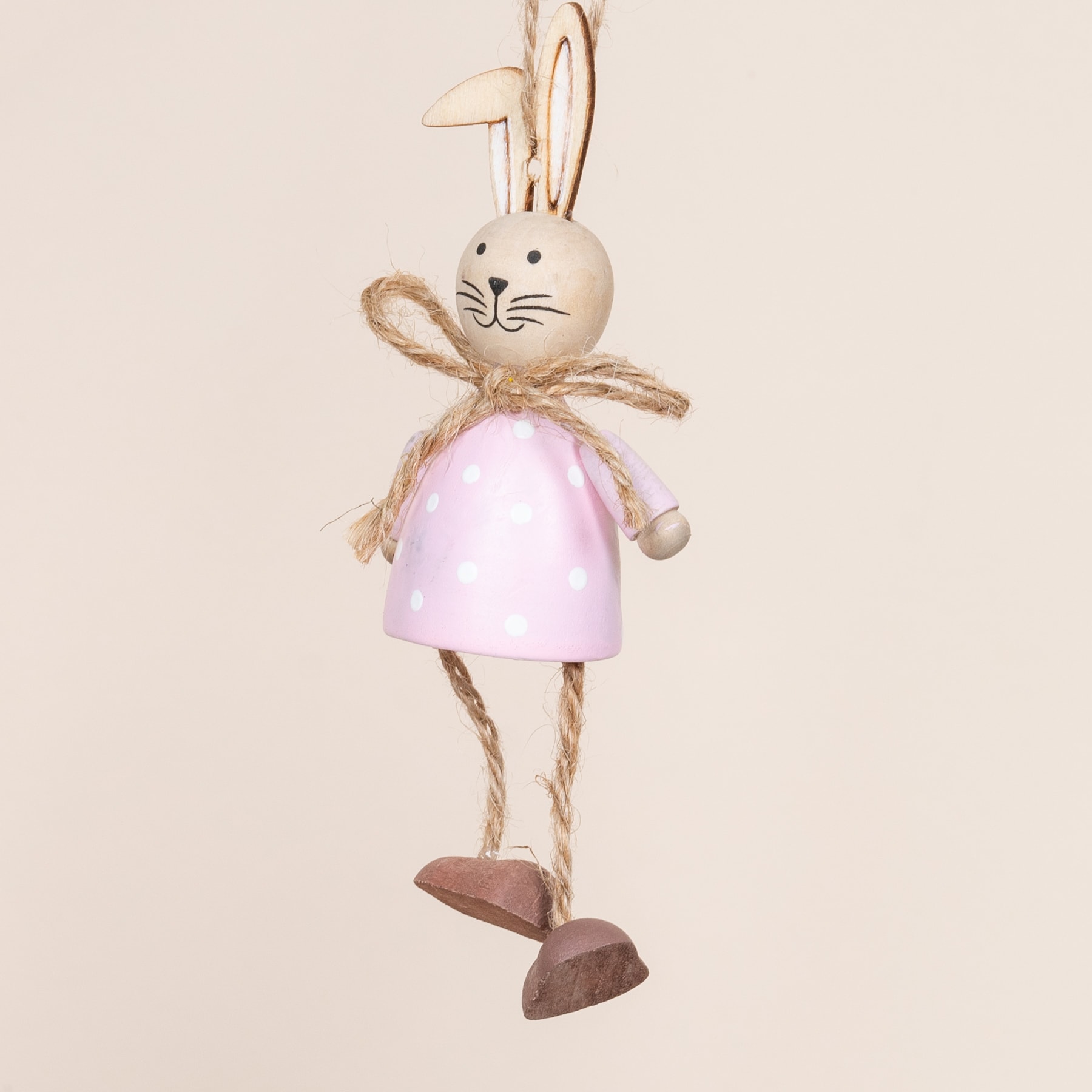Eine hölzerne Hasenfigur mit einem rosa Kleid und einer Fliege, die auf einem beigen Hintergrund steht.
