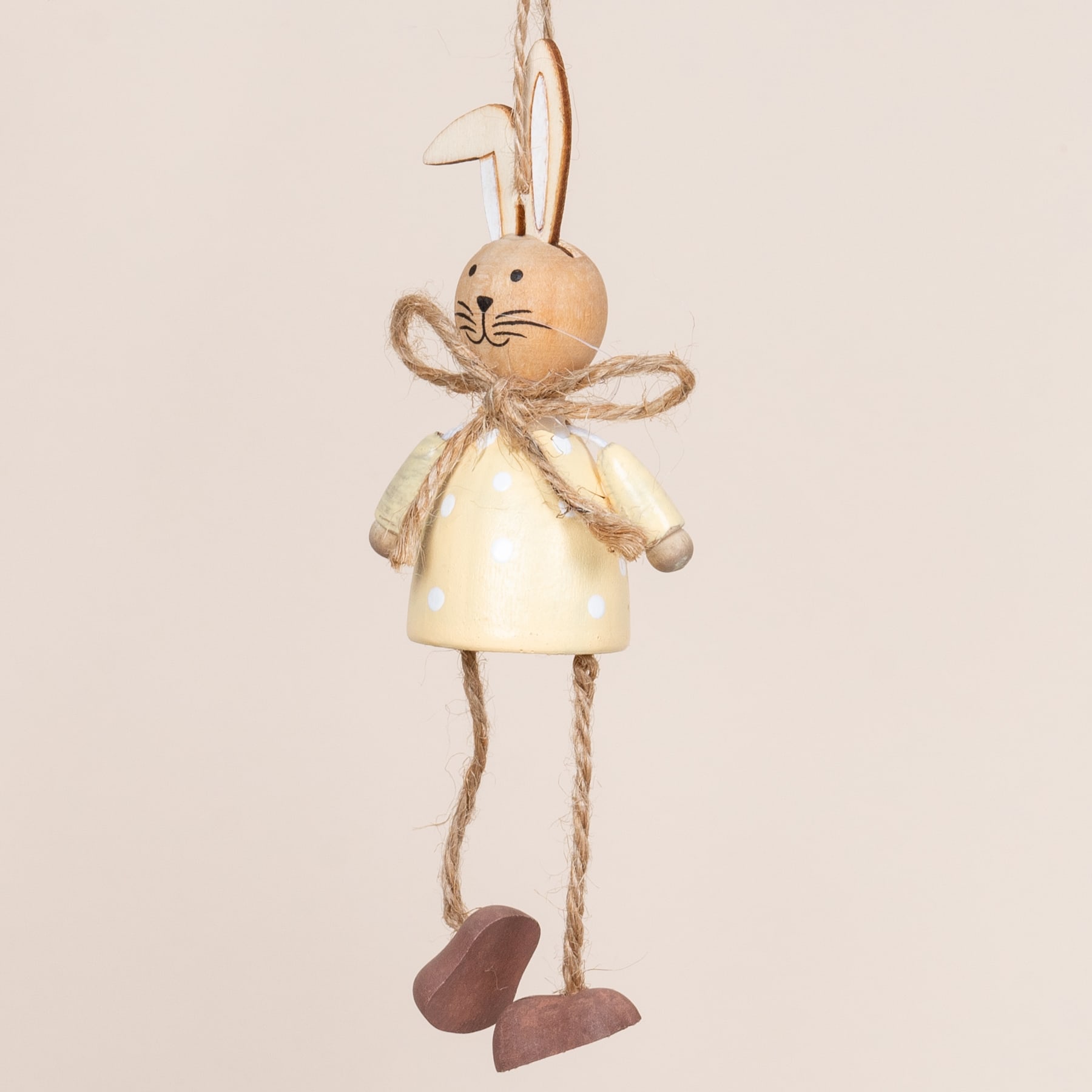 Eine süße, plüschige Kaninchenfigur mit gelbem Kleid und Seilbeinen steht vor einem schlichten, beigen Hintergrund.