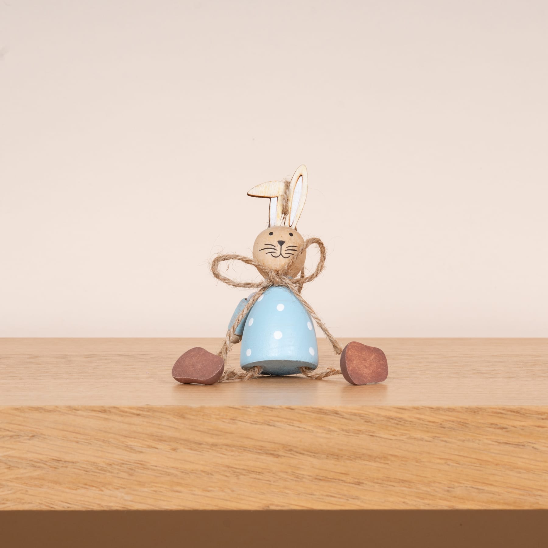 Eine hölzerne Tischoberfläche, auf der eine skurrile, kaninchenförmige Figur mit einem blauen, glockenförmigen Körper und hölzernen Gliedmaßen sitzt.