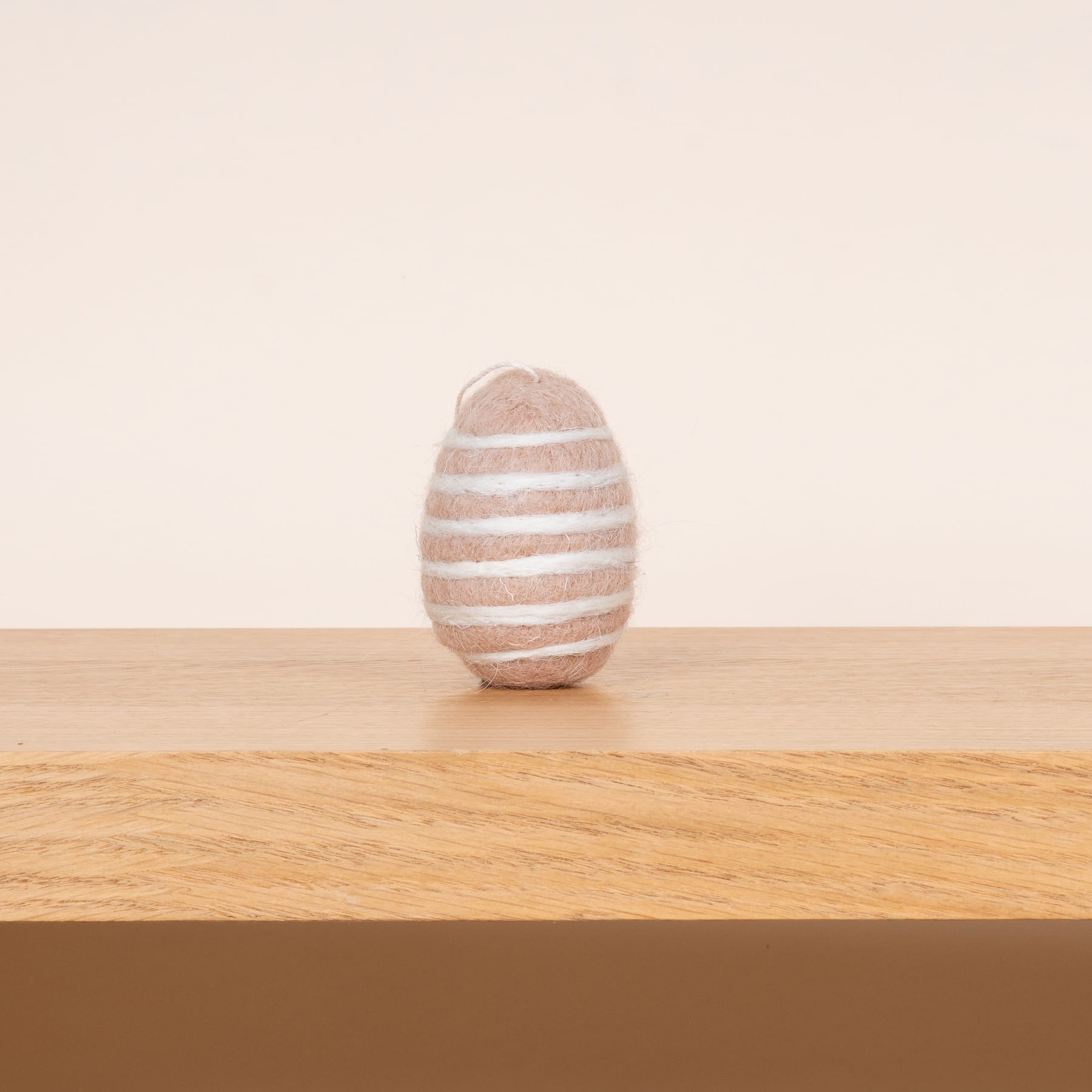 Ein gestreiftes eiförmiges Objekt aus Stein liegt auf einer Holzoberfläche vor einem schlichten beigen Hintergrund.