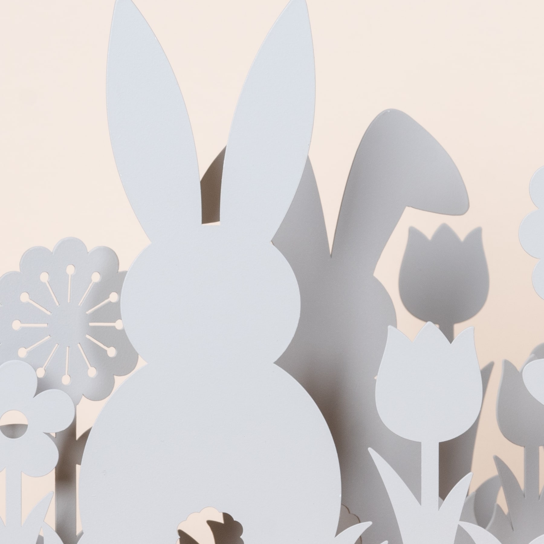 Das Bild zeigt ein minimalistisches, abstraktes Design mit verschiedenen weißen und grauen Formen, die einem Kaninchen, Blumen und anderen organischen Formen vor einem hellen Hintergrund ähneln.