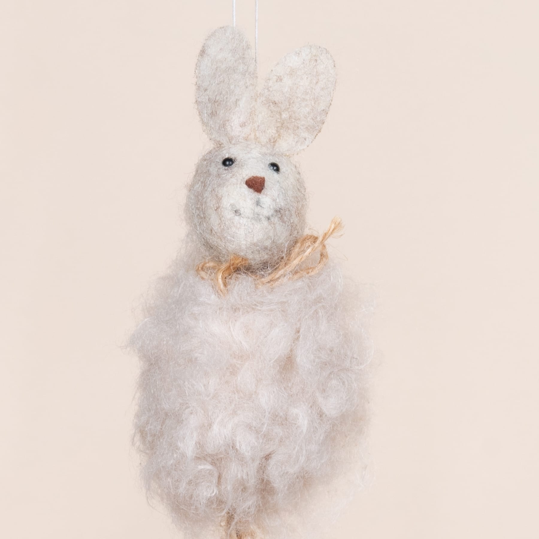 Ein weiches, flauschiges weißes Plüschkaninchen mit schwarzen Augen und einer Fliege sitzt vor einem schlichten beigen Hintergrund.