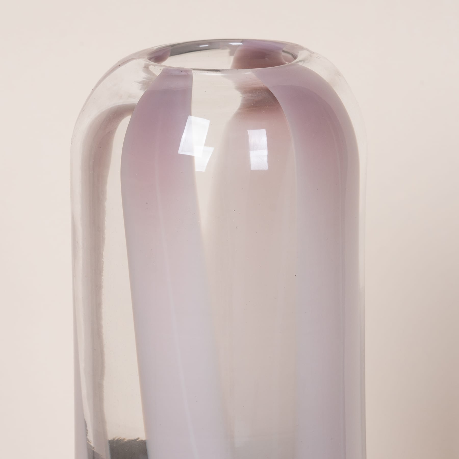 Eine Glasvase in einem blassen Rosaton steht vor einem neutralen Hintergrund und zieht mit ihrer schlichten, aber eleganten Form die Aufmerksamkeit auf sich.
