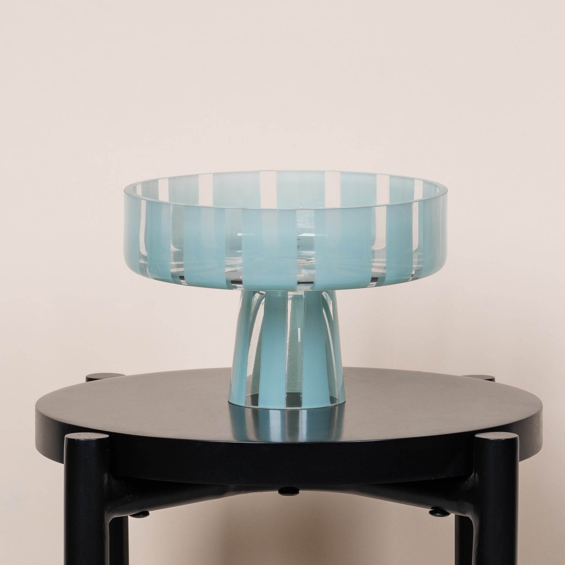 Ein Glassockel mit einer transparenten, schalenförmigen Oberseite steht auf einem schwarzen, runden Sockel vor einem hellen Hintergrund.