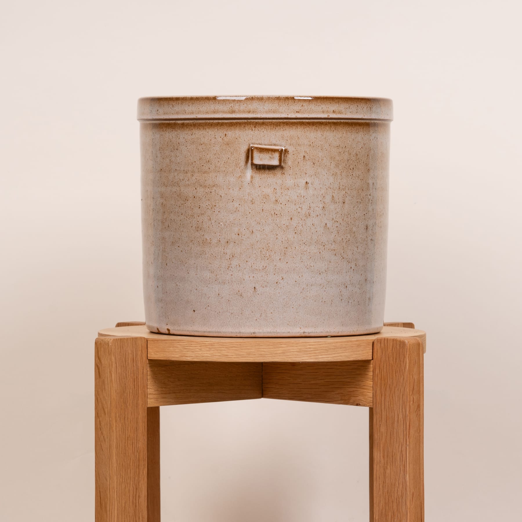 Auf einem schlichten Hintergrund steht ein Keramiktopf mit Holzständer.