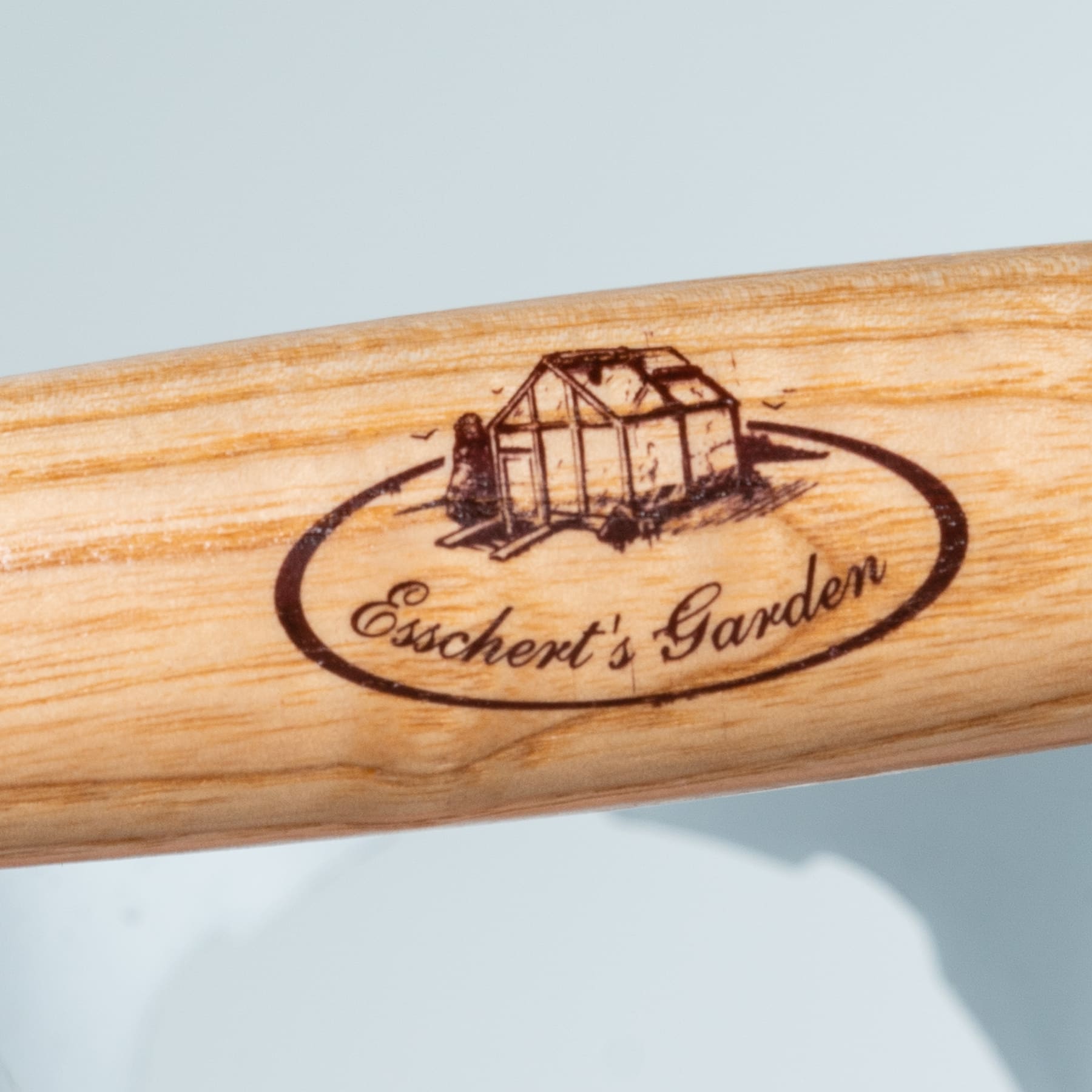 Eine Holzoberfläche mit eingebranntem Bild einer kleinen Gewächshauskonstruktion und dem eingravierten Text „Eischerts Garten“.